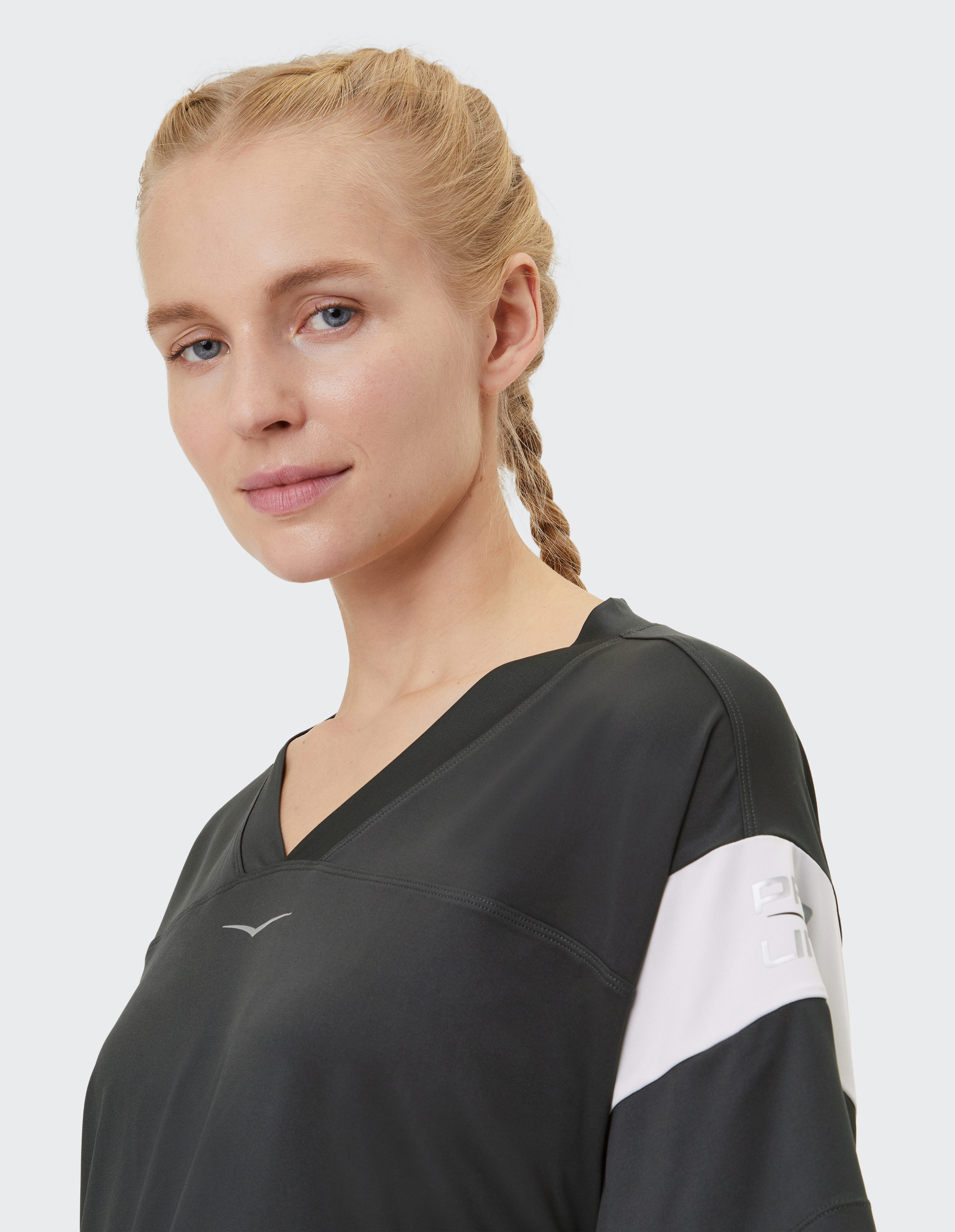 Frau mit blonden, geflochtenen Haaren trägt ein schwarzes V-Ausschnitt-Shirt mit weißem Streifen, lächelt leicht und schaut zur Seite.