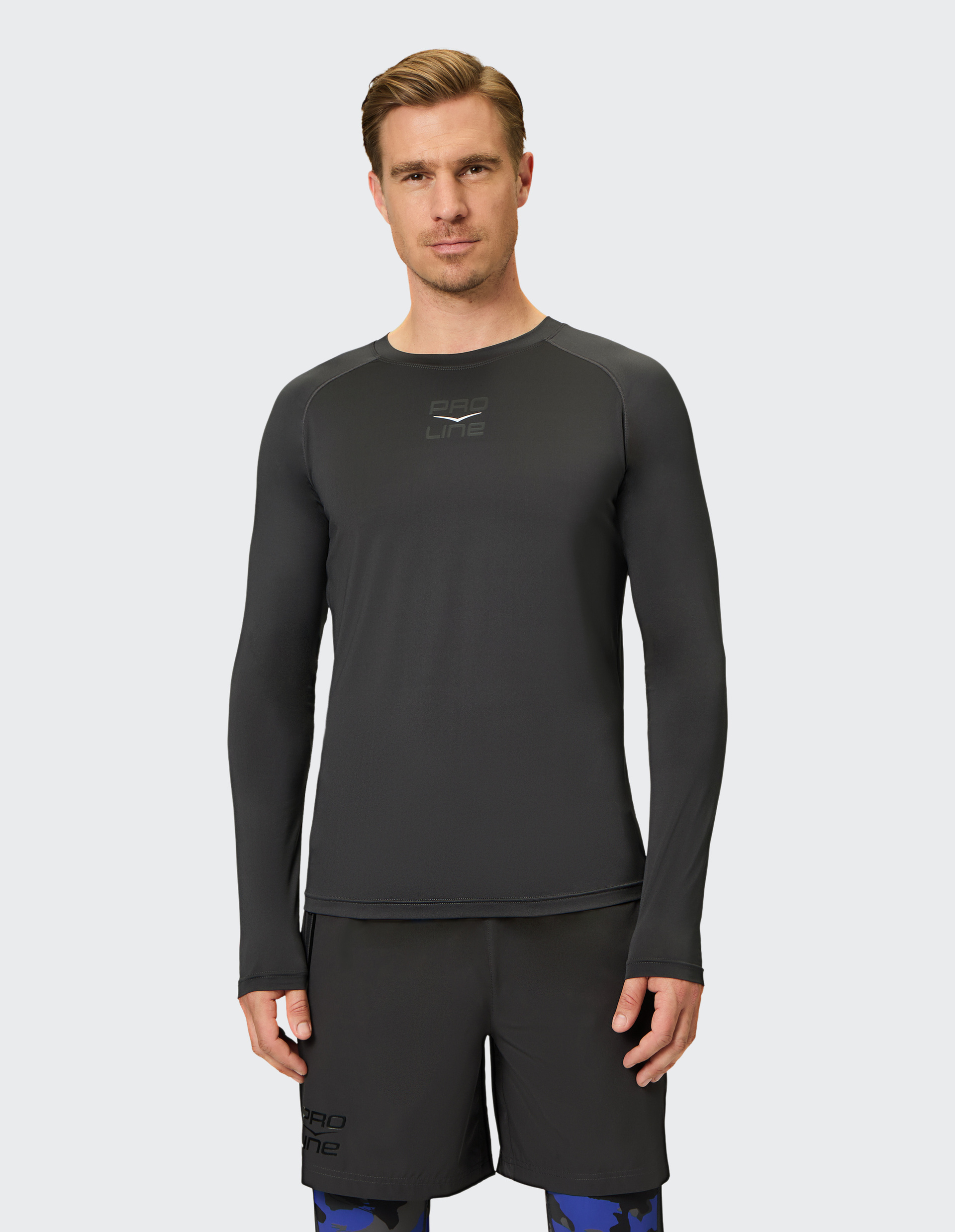 Mann in sportlichem, schwarzem Langarmshirt und Shorts vor grauem Hintergrund, blickt direkt in die Kamera.