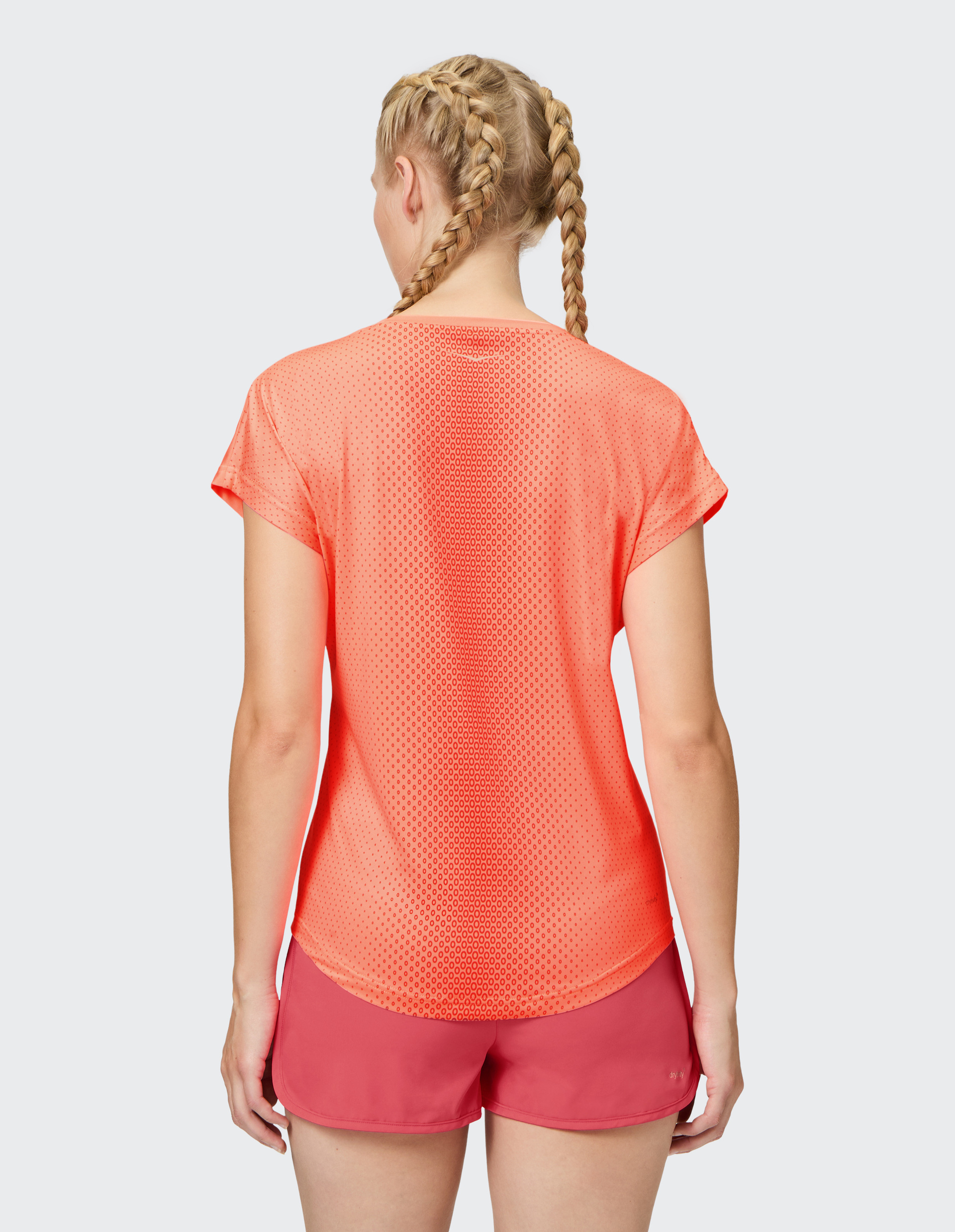 Frau mit zwei geflochtenen Zöpfen trägt ein orangefarbenes, transparentes Sportshirt und rosa Shorts, Rückansicht.