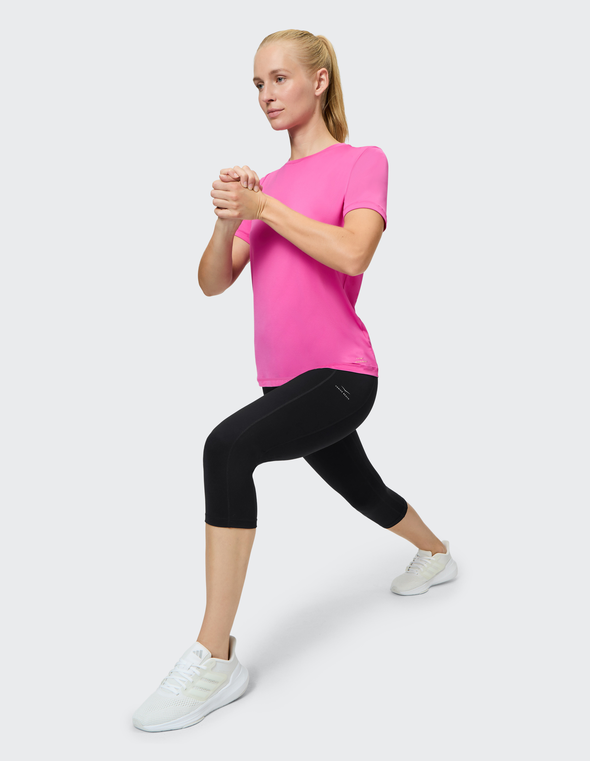 Eine Frau in einem pinken T-Shirt und schwarzen Leggings macht einen Ausfallschritt, ihre Haare sind zu einem Pferdeschwanz gebunden.