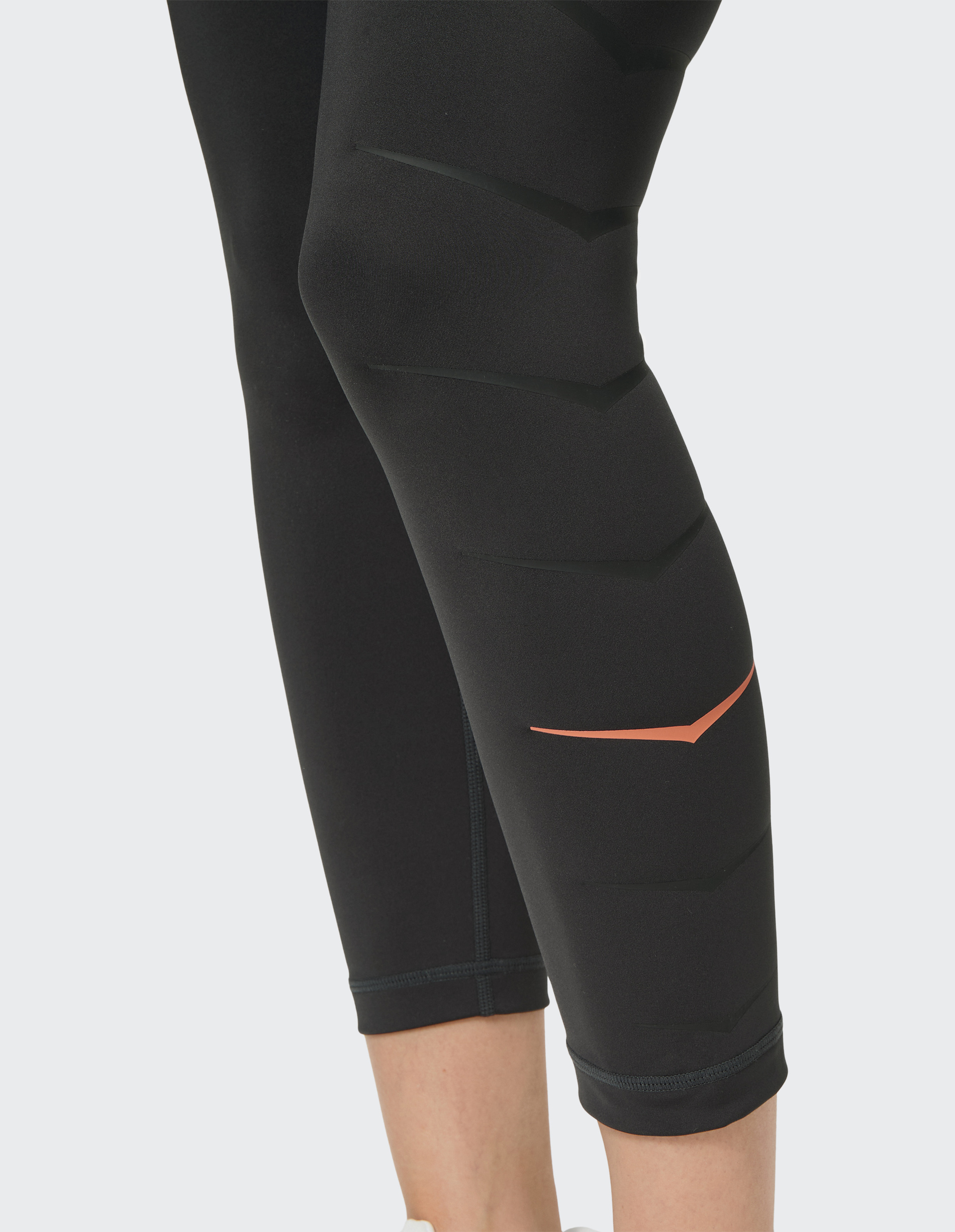 Schwarze Sportleggings mit dezentem Chevron-Muster und rotem Akzent am Bein, die einen Teil der Waden zeigt.