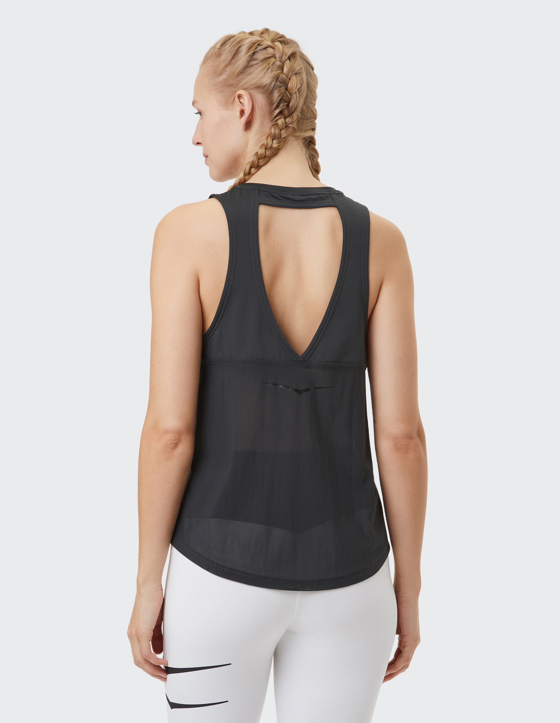 Eine Frau mit geflochtenem Haar trägt ein schwarzes ärmelloses Top mit offenem Rückenausschnitt und weiße Leggings.