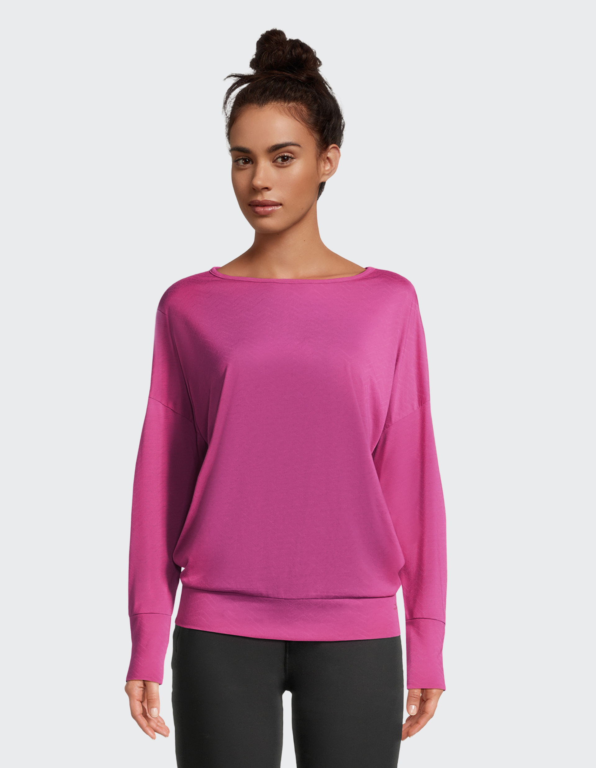 Eine Frau trägt ein locker sitzendes, pinkes Oberteil und schwarze Leggings, ihre Haare sind zu einem Dutt gebunden.