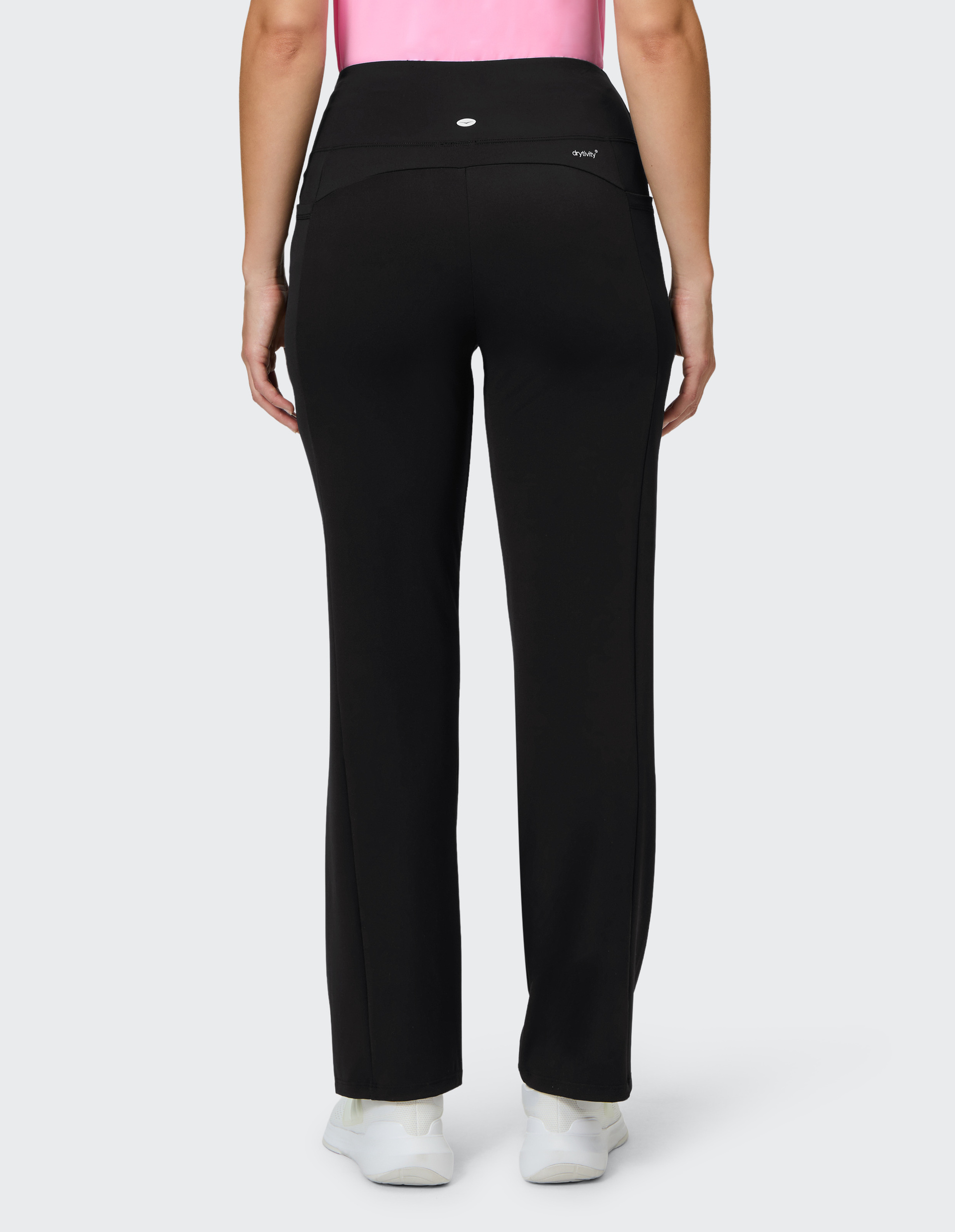 Eine Person in schwarzen Sporthosen steht rückwärts, trägt weiße Sneaker und ein pinkes Top auf grauem Hintergrund.