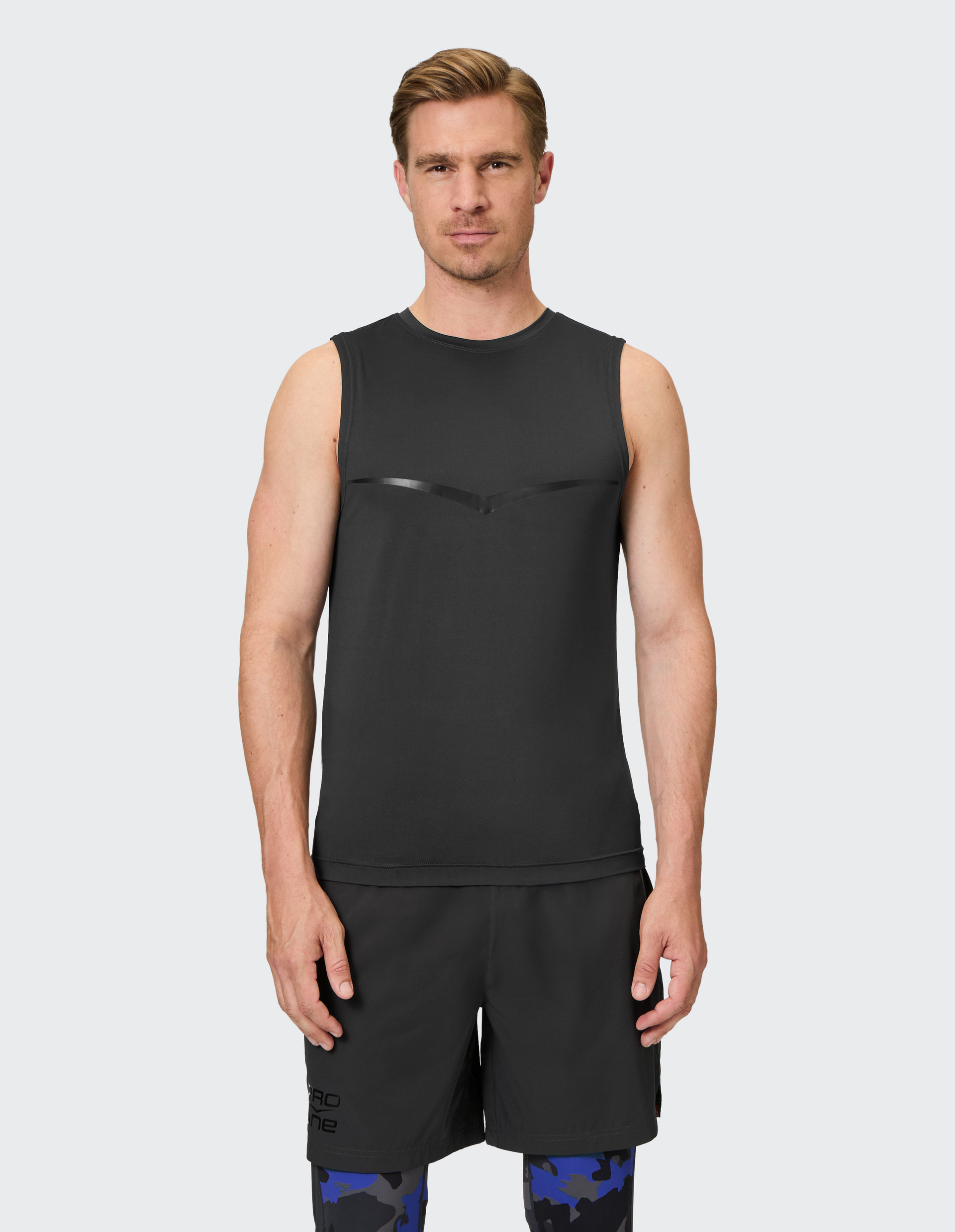 Ein Mann trägt ein ärmelloses, schwarzes Sportshirt und Shorts mit blauen Tarnmuster-Leggings, steht vor einem neutralen Hintergrund.