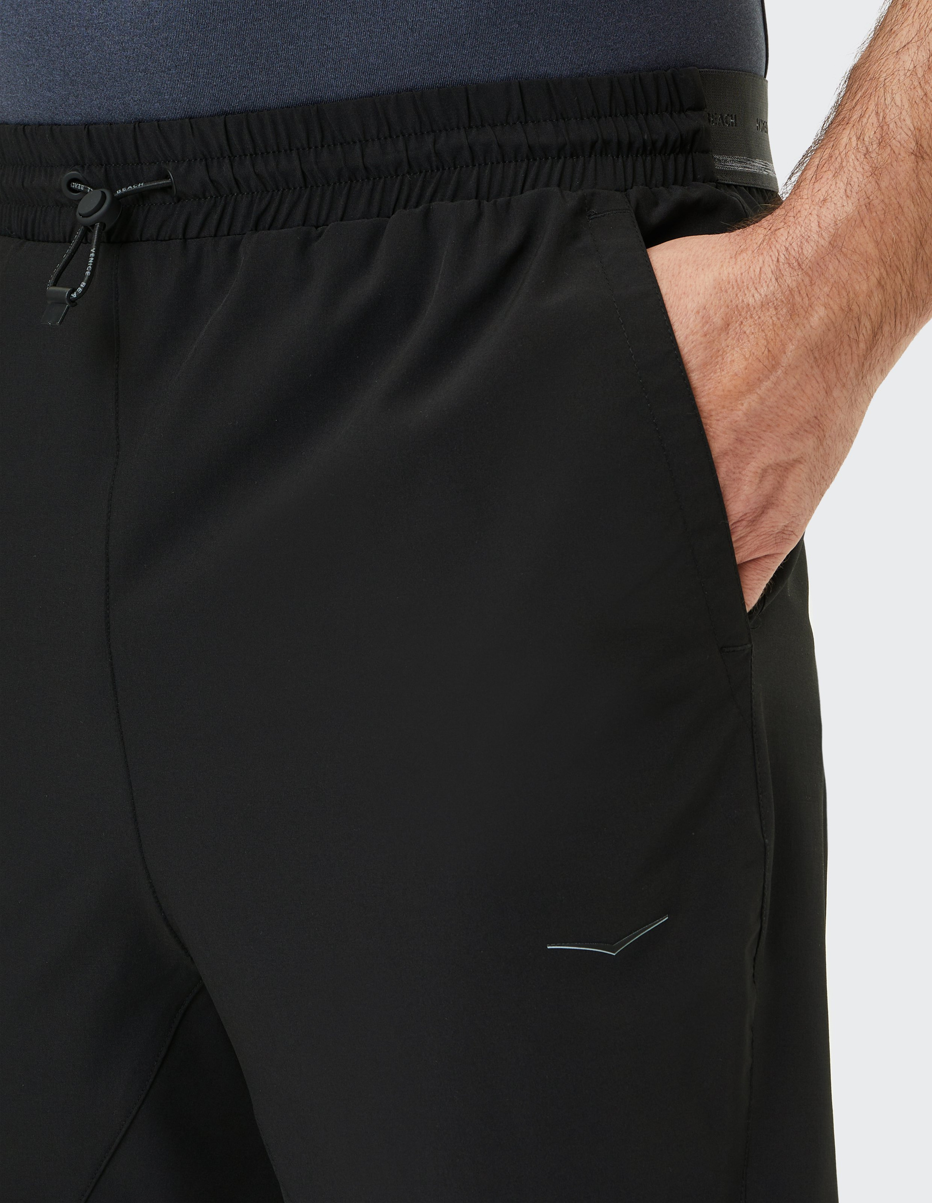 Nahaufnahme einer schwarzen Sporthose mit elastischem Bund und seitlicher Tasche, in der eine Hand steckt.
