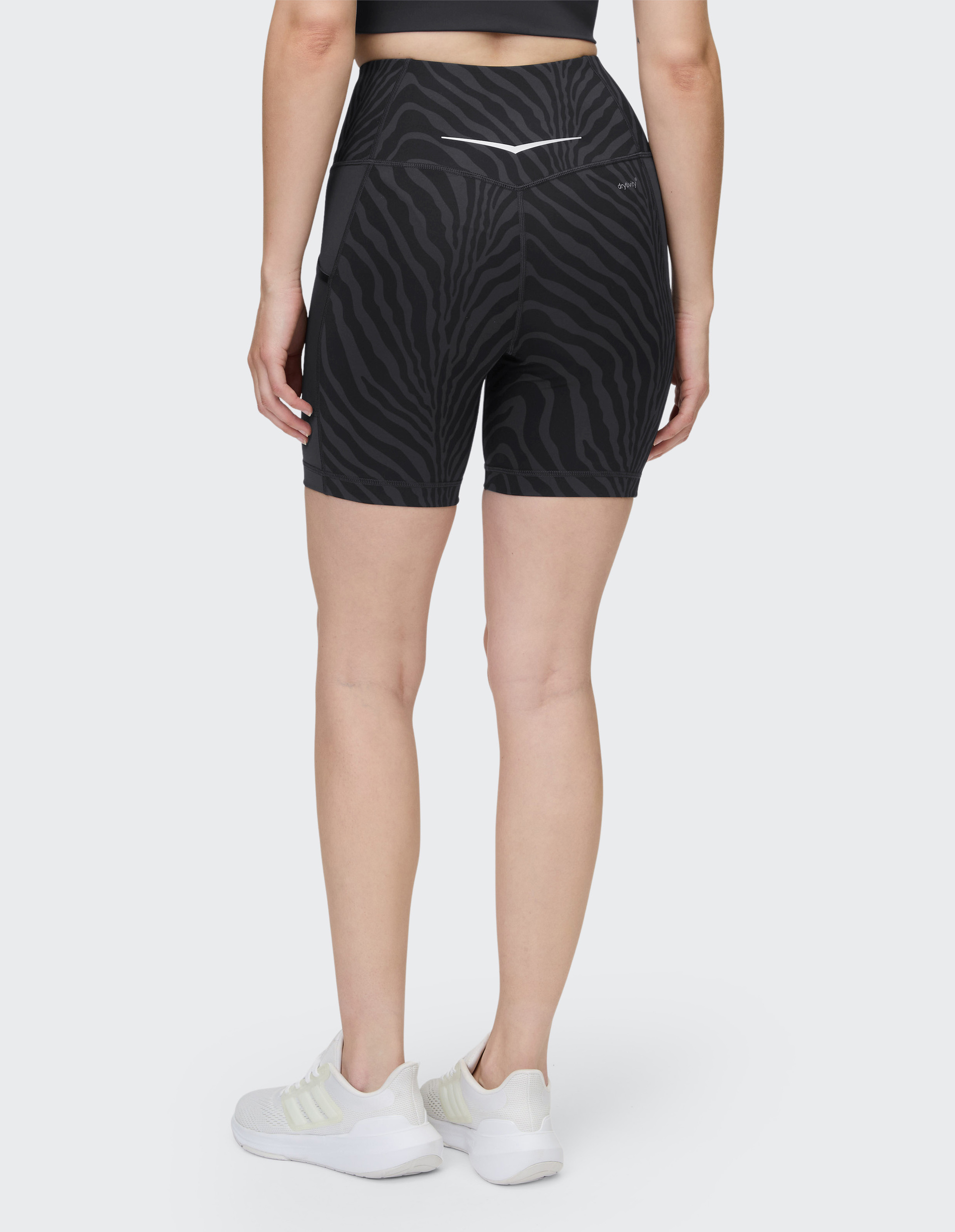 Rückansicht einer Person in schwarzer, gemusterter Sporthose und weißem Sporttop, die weiße Turnschuhe trägt.