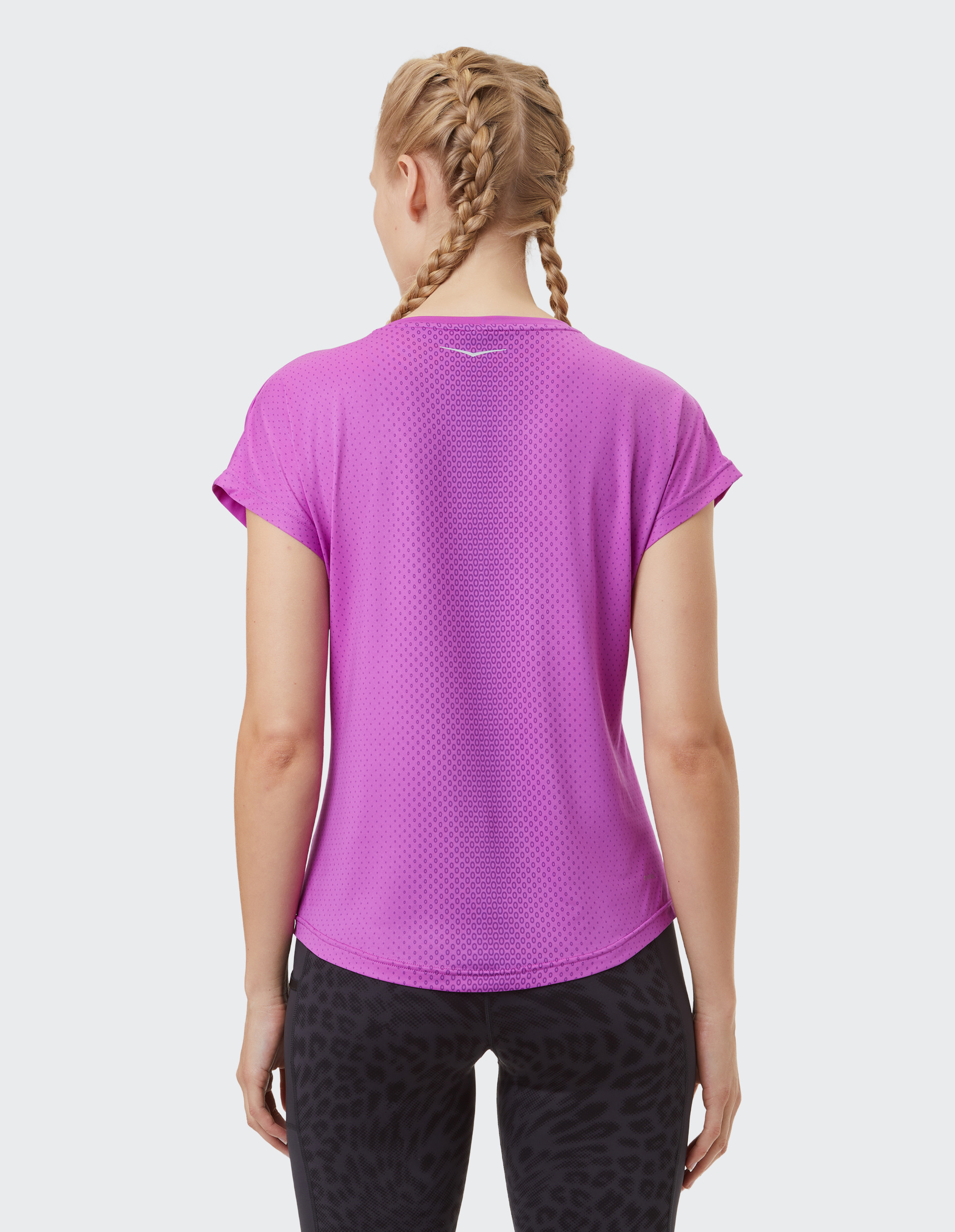 Eine Frau mit zwei Zöpfen trägt ein lila Sportshirt und schwarze Muster-Leggings, von hinten fotografiert.