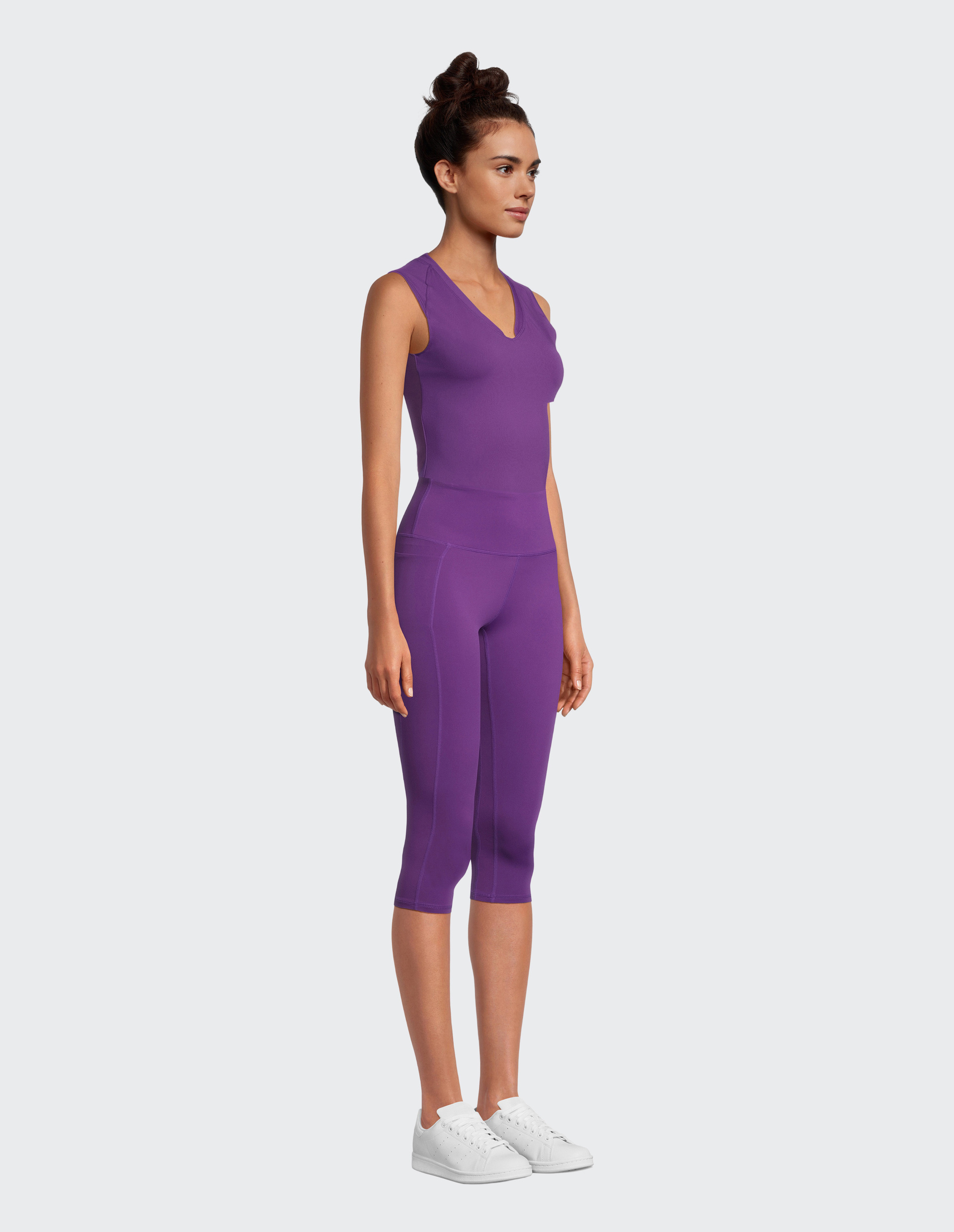 Eine Frau trägt ein lilafarbenes, ärmelloses V-Ausschnitt-Oberteil und passende Dreiviertel-Leggings.