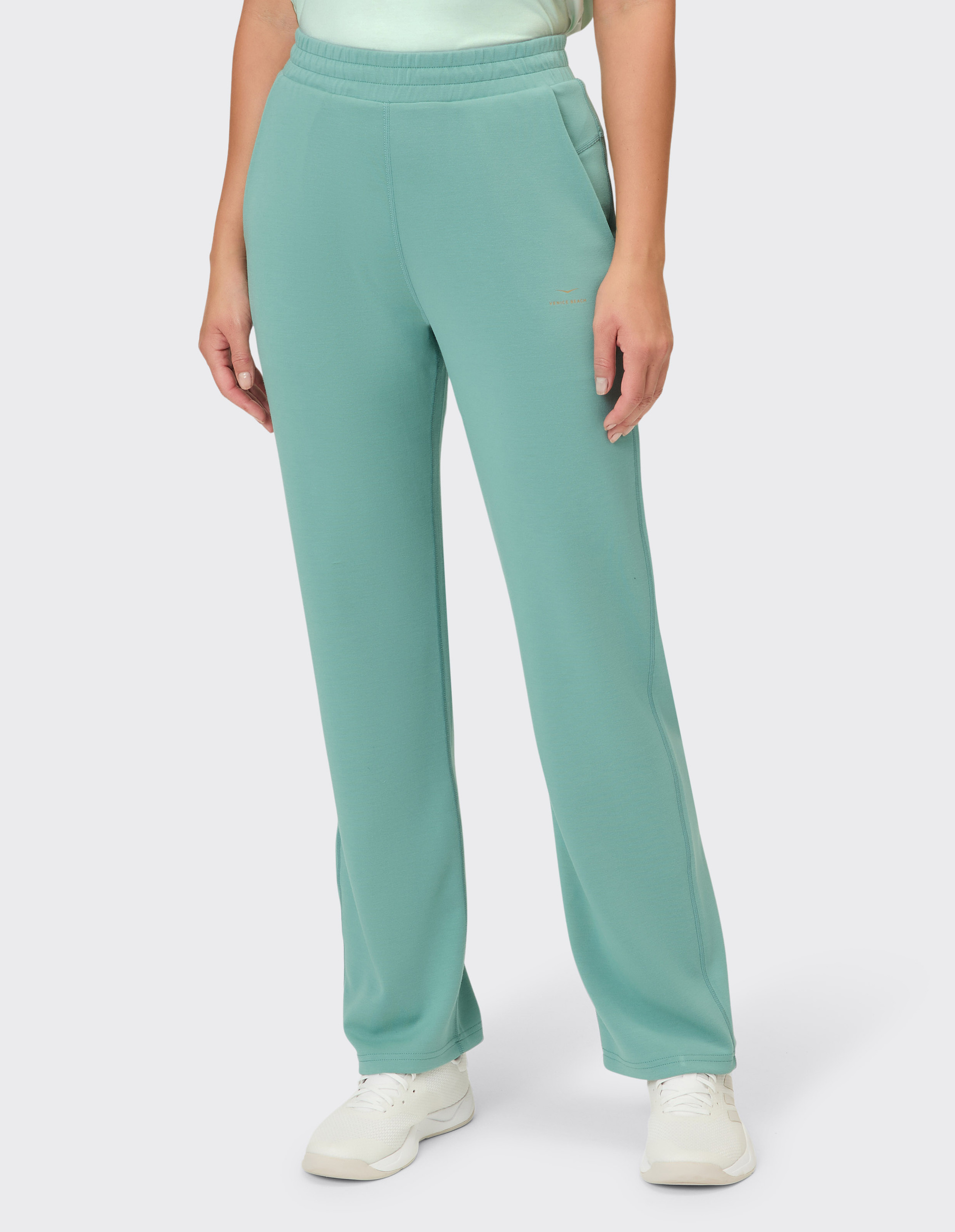 Eine Frau trägt eine türkise, gerade geschnittene Hose mit Eingrifftaschen und einem kleinen Logodetail.