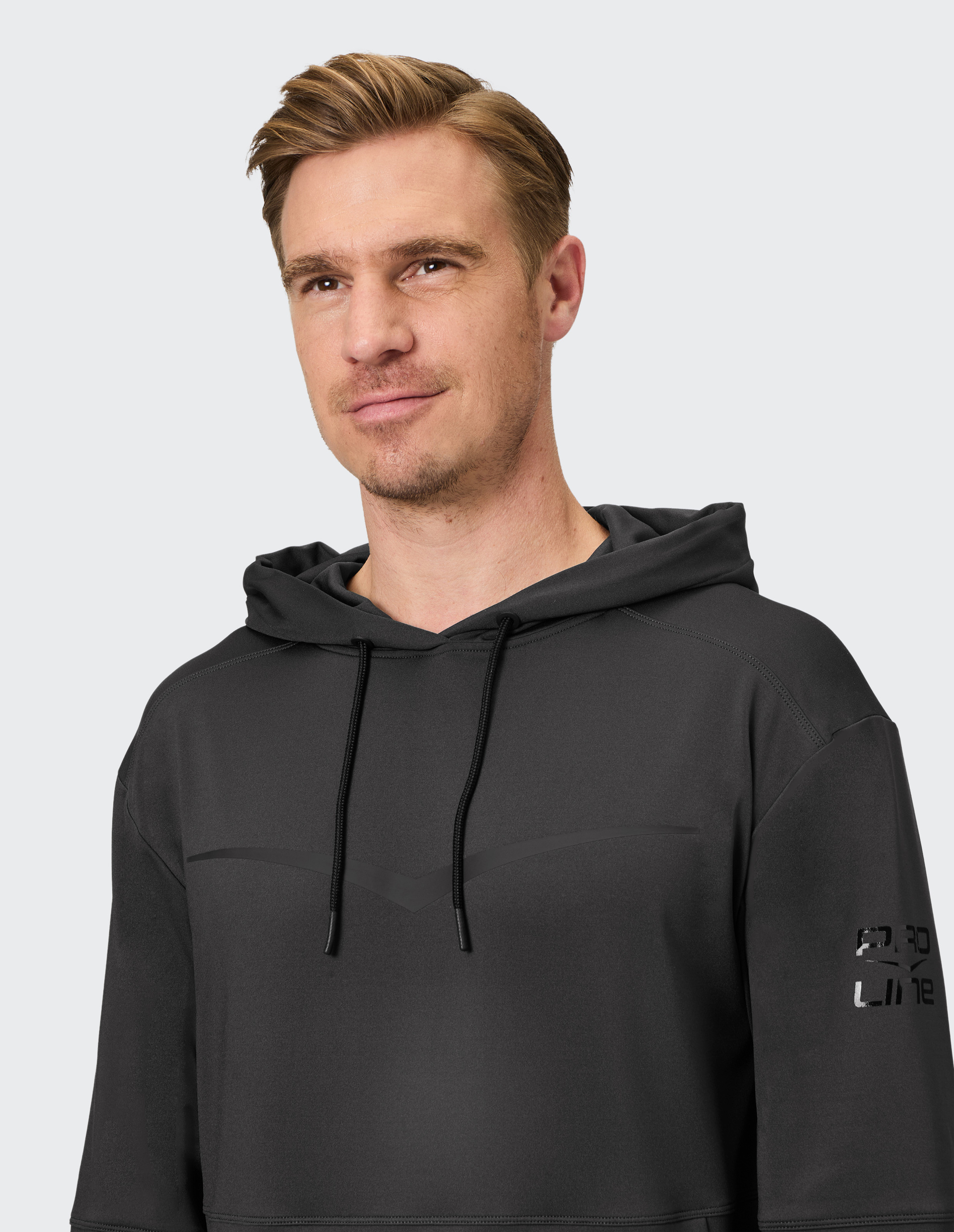 Mann mit kurzen Haaren trägt schwarzen Kapuzenpullover mit Druck auf Ärmel vor hellem Hintergrund und blickt freundlich zur Seite.