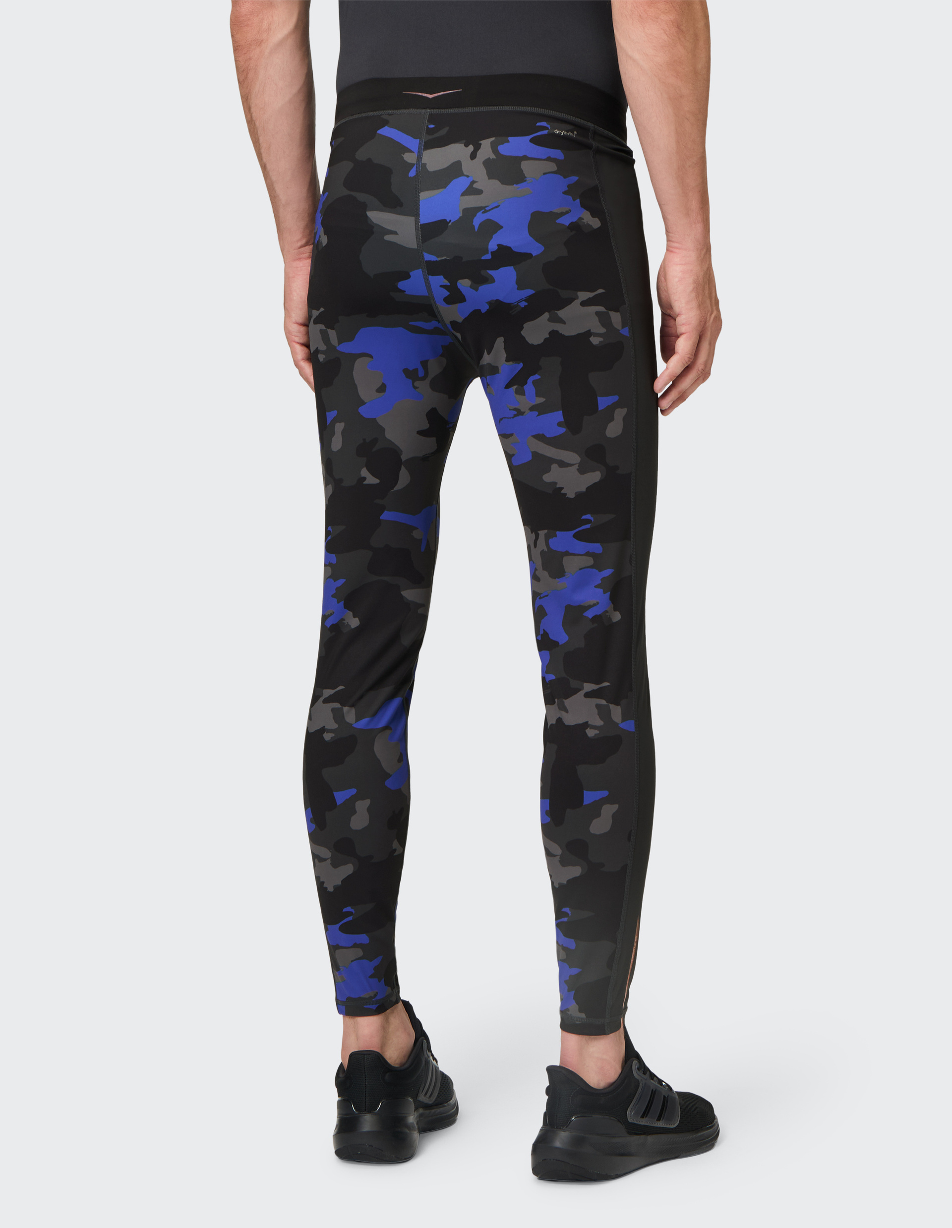 Ein Mann in Taillenkameraperspektive trägt enge Leggings mit blau-schwarzem Camouflage-Muster und schwarzen Sportschuhen.