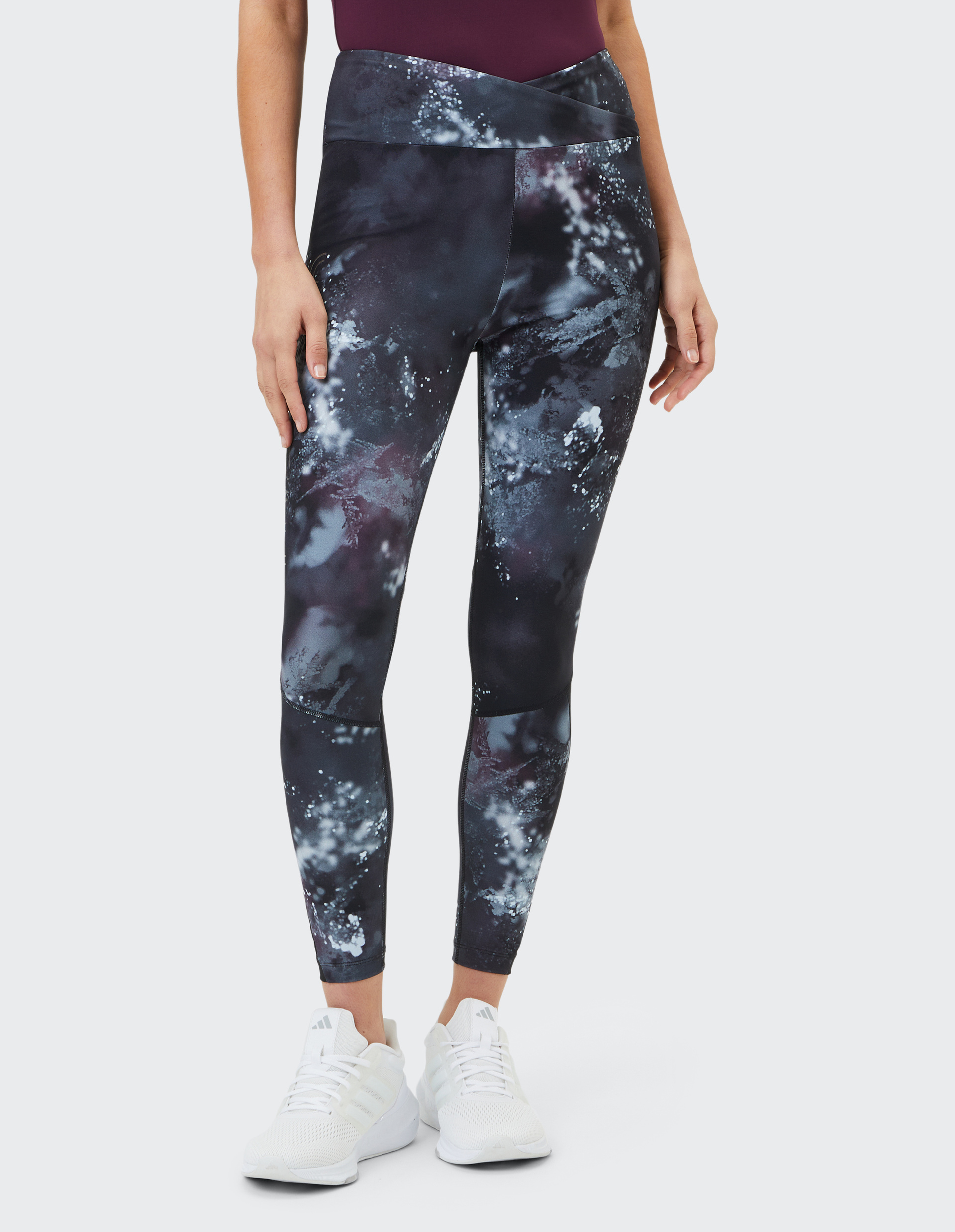 Frau trägt Leggings mit galaktischem Muster, das dunkle und helle Flecken zeigt, kombiniert mit weißen Turnschuhen auf hellem Hintergrund.