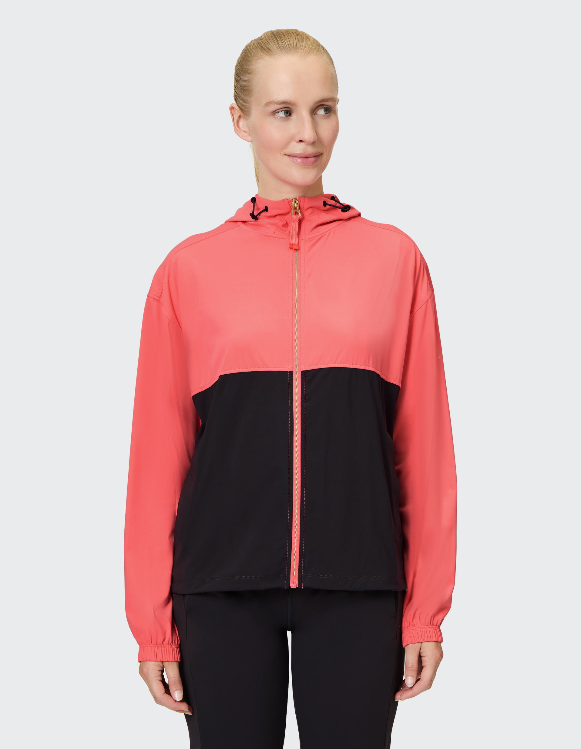 Eine Person trägt eine zweifarbige Jacke mit rosem oberen Teil und schwarzem unteren Bereich, dazu passende schwarze Leggings.