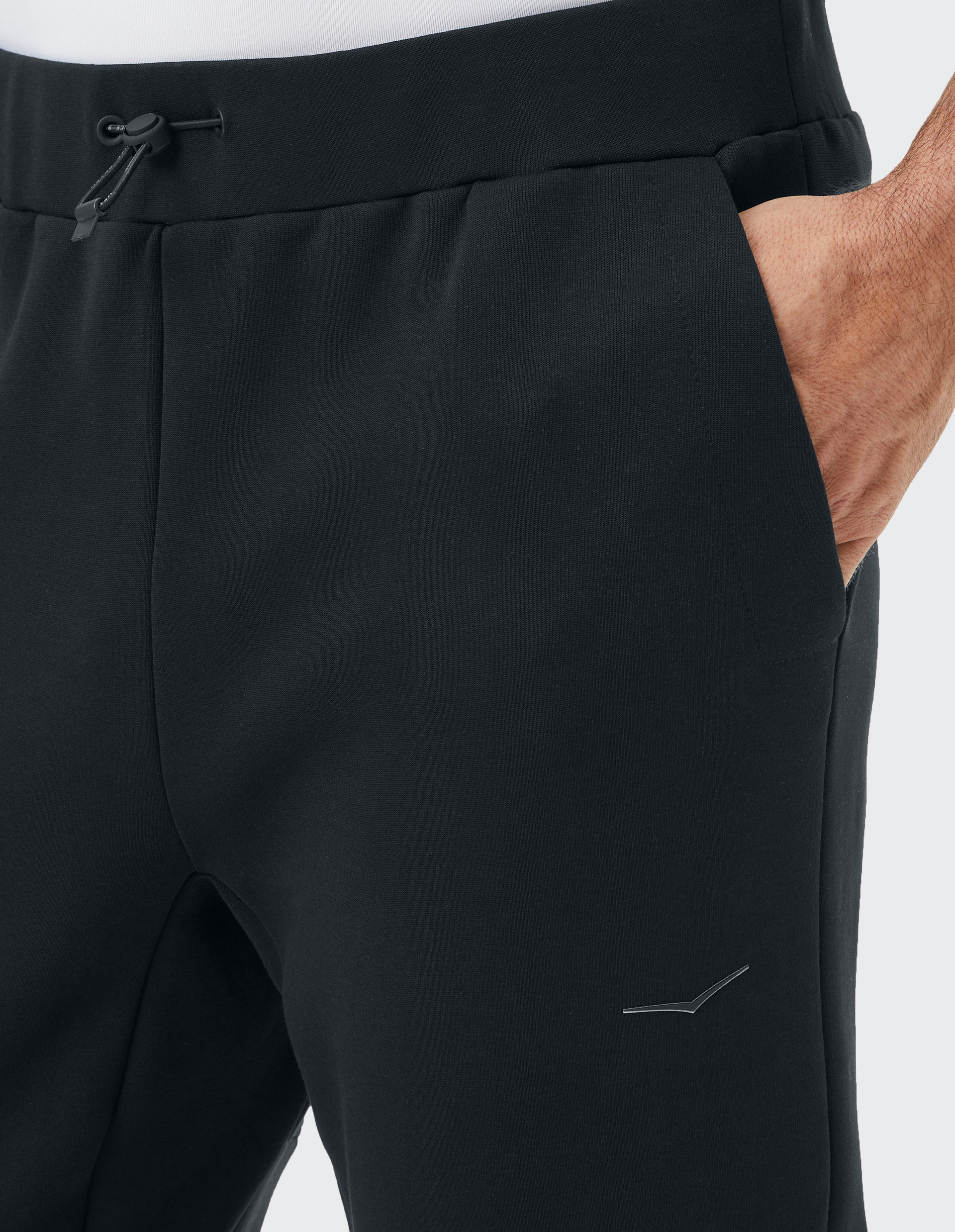 Schwarze Jogginghose mit elastischem Bund und Kordelzug. Eine Hand steckt lässig in der rechten Hosentasche, kleines Logo sichtbar.