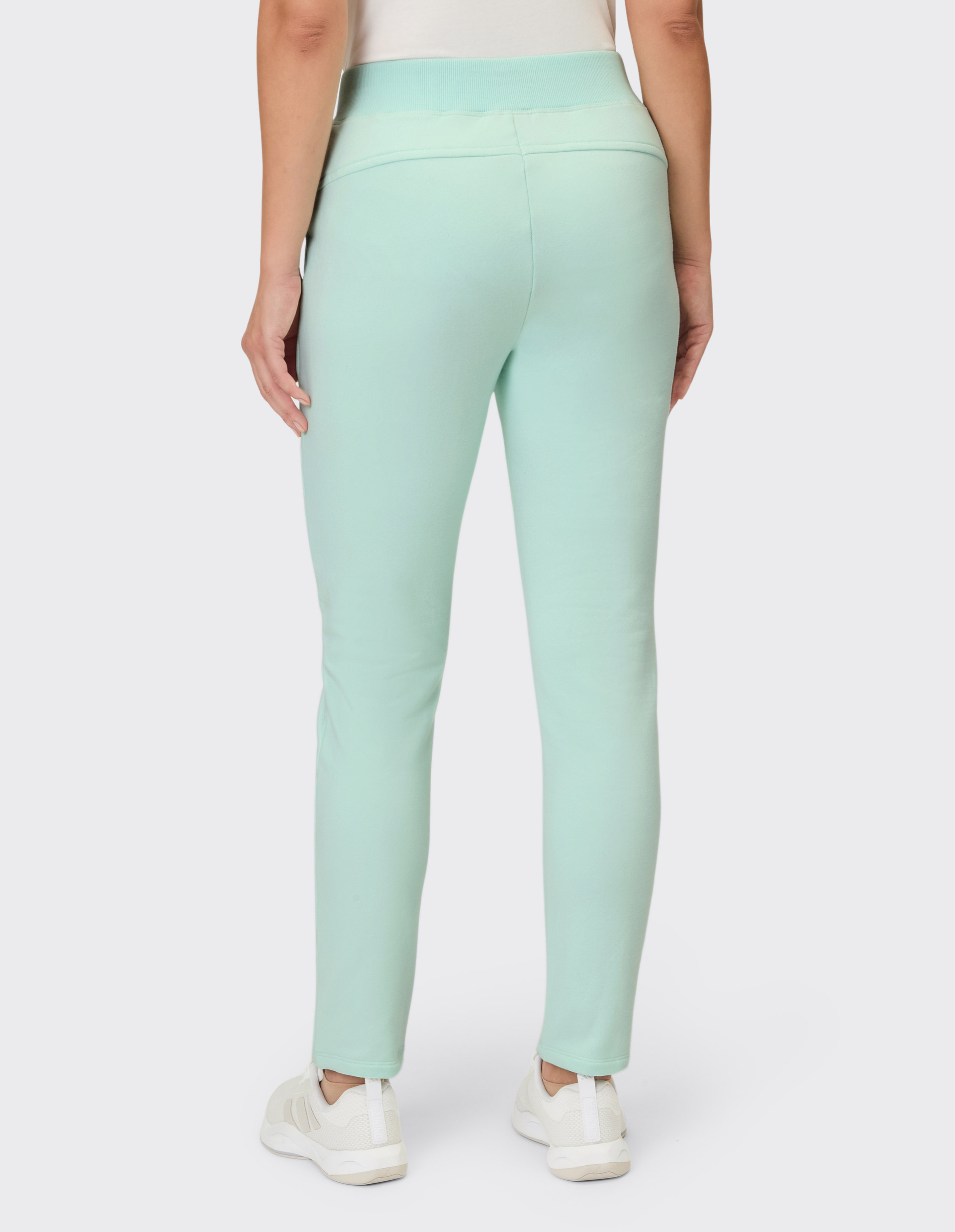 Eine Person trägt eine leichte Minzgrüne Hose mit elastischem Bund und sportliche weiße Sneakers.