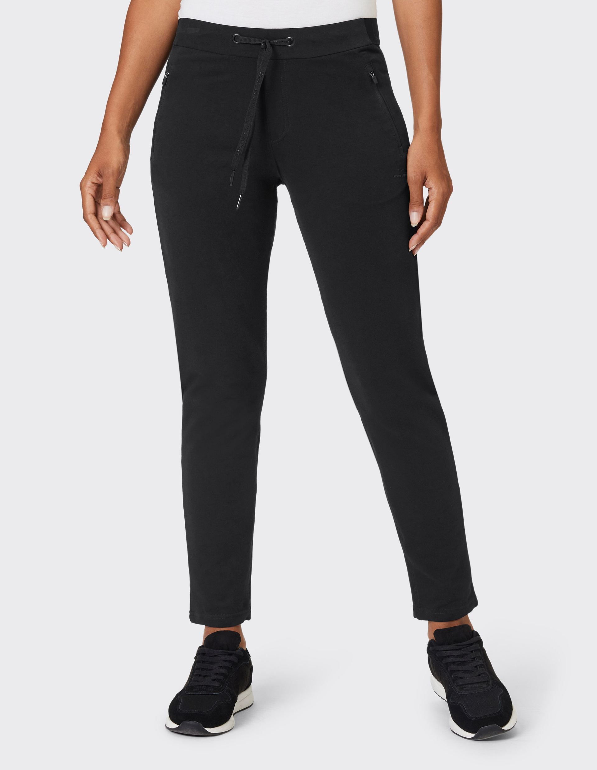 Eine Person trägt schwarze Jogginghosen mit Kordelzug und schwarzen Sneakers auf hellem Hintergrund.