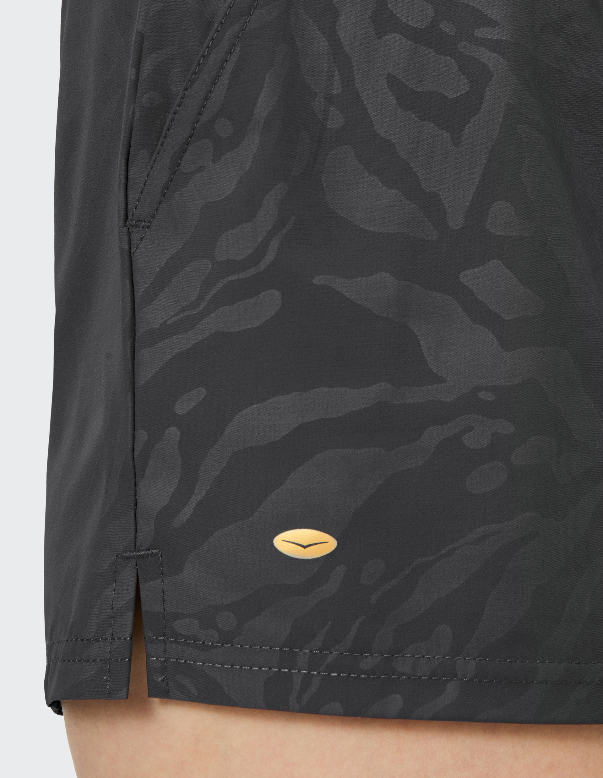 Nahaufnahme eines dunklen Stoffmusters mit einem dezenten, abstrakten Design und einem kleinen, ovalen, goldenen Logo in der Mitte.