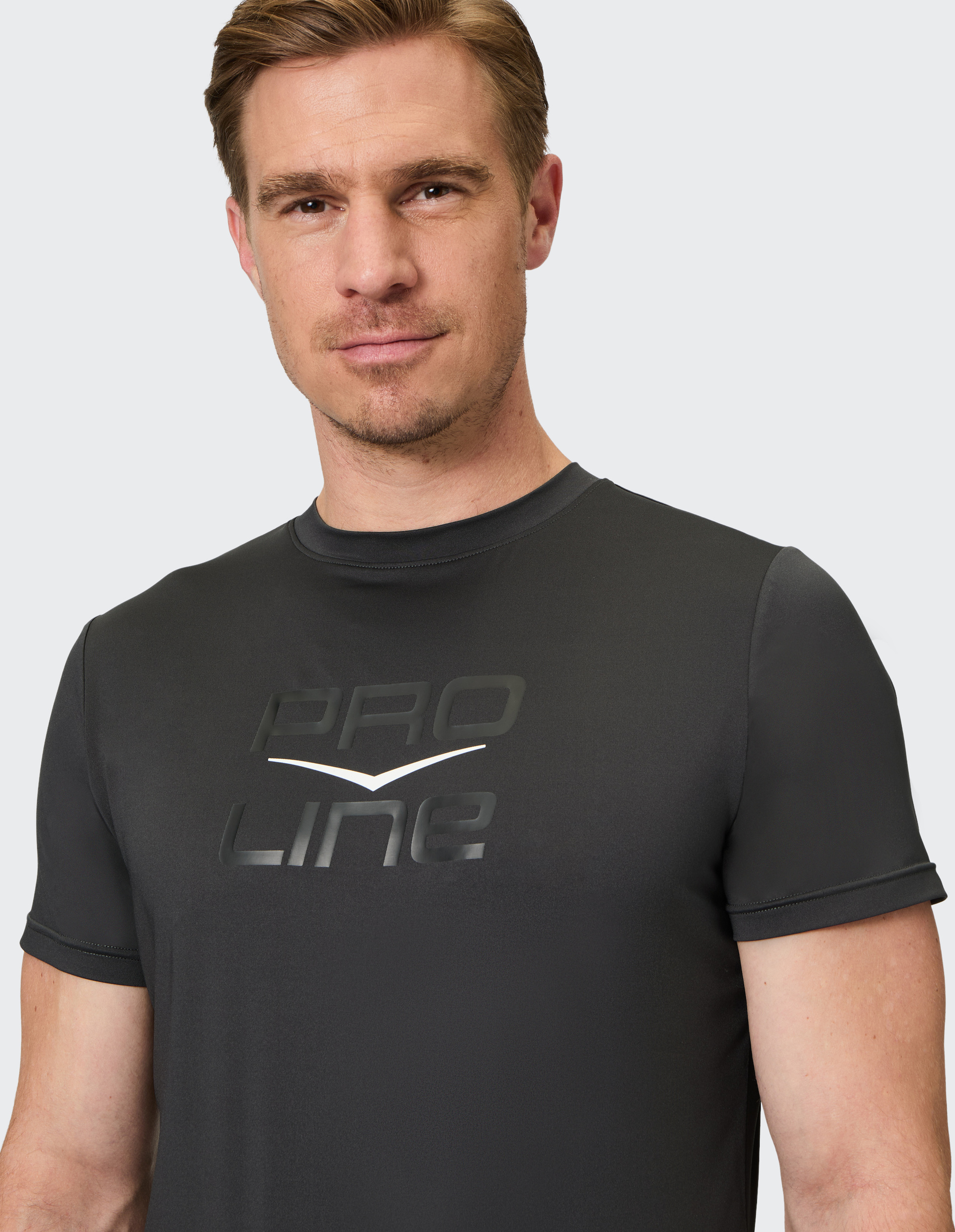 Ein Mann mit kurzem Haar trägt ein schwarzes T-Shirt mit der Aufschrift "Pro Line" und blickt direkt in die Kamera.