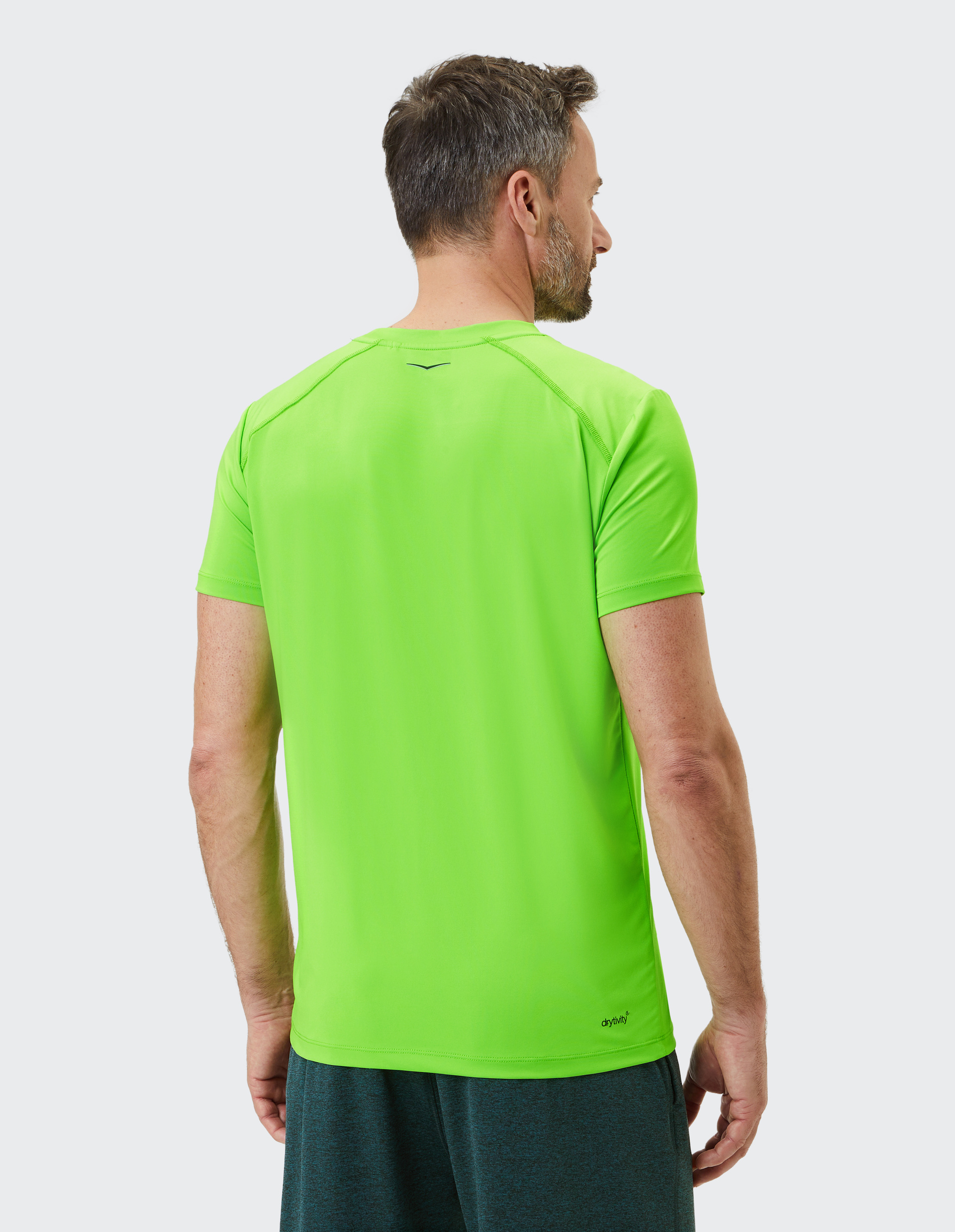 Ein Mann in einem leuchtend grünen T-Shirt und dunklen Shorts steht rückwärts, mit Blick nach rechts.