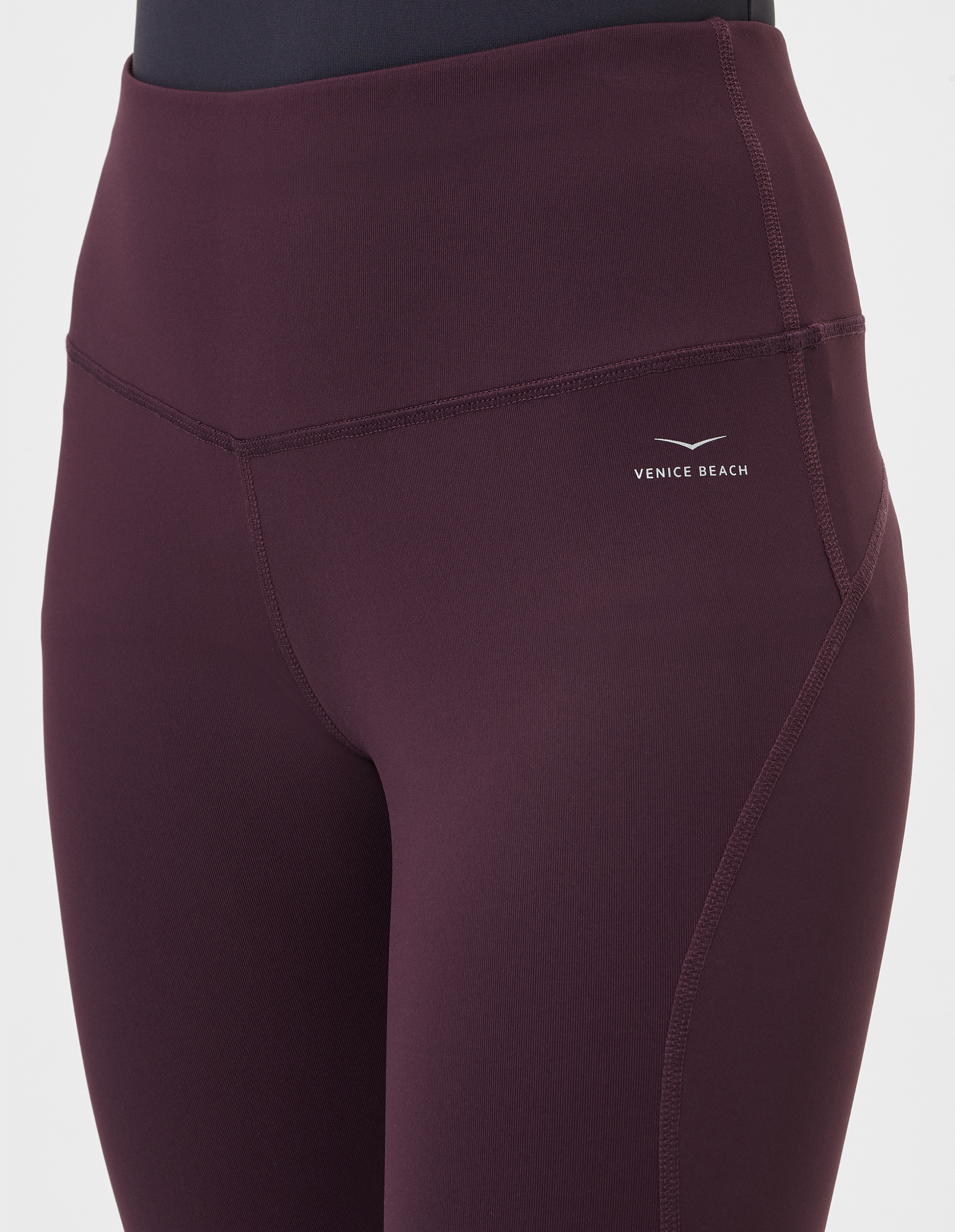 Nahaufnahme einer dunkelroten Sportleggings mit hoher Taille und dezentem Markenlogo auf dem Oberschenkel vor weißem Hintergrund.