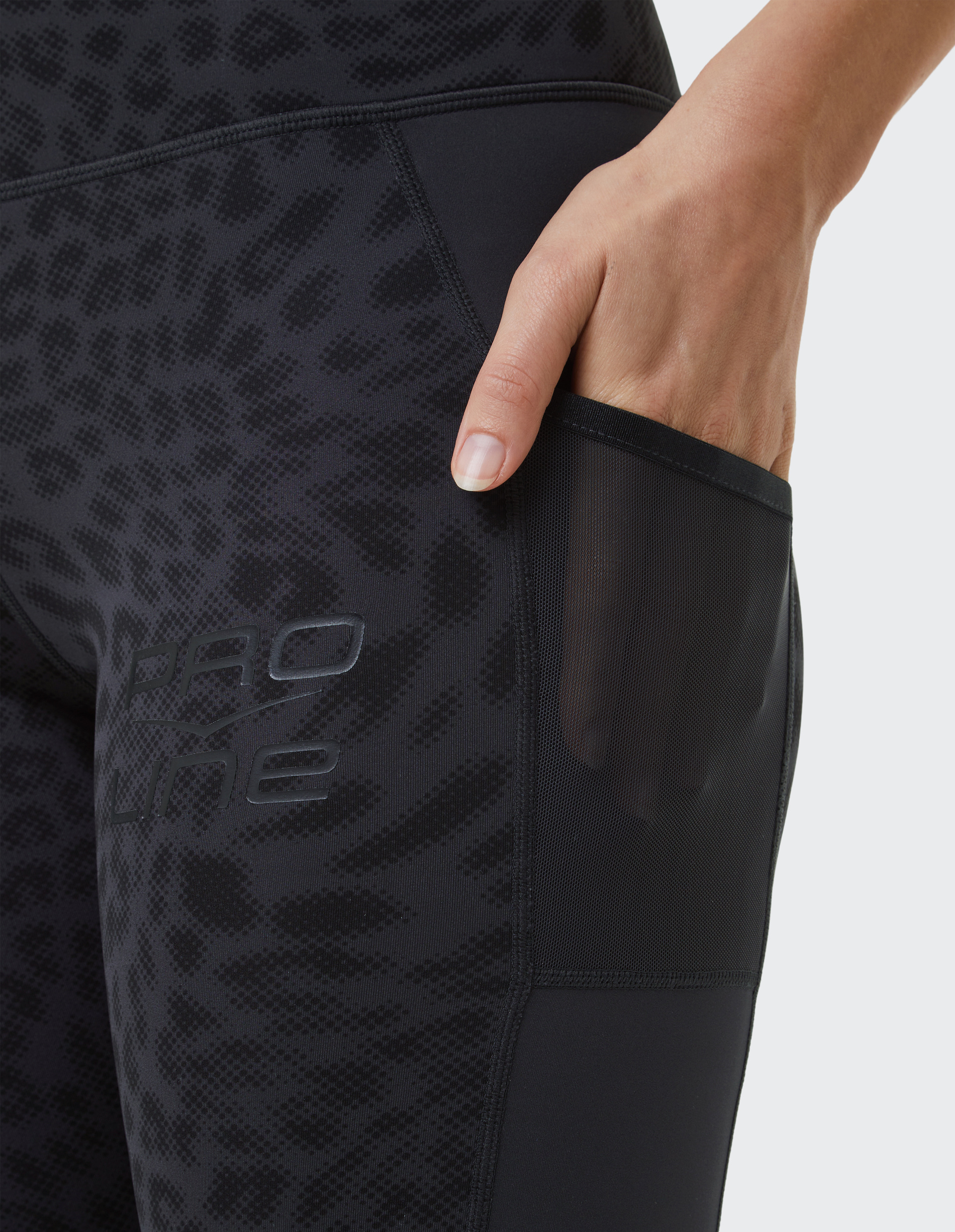 Nahaufnahme einer schwarzen Sportleggings mit dezentem Leopardenmuster und einer Hand, die eine transparente Seitentasche nutzt.