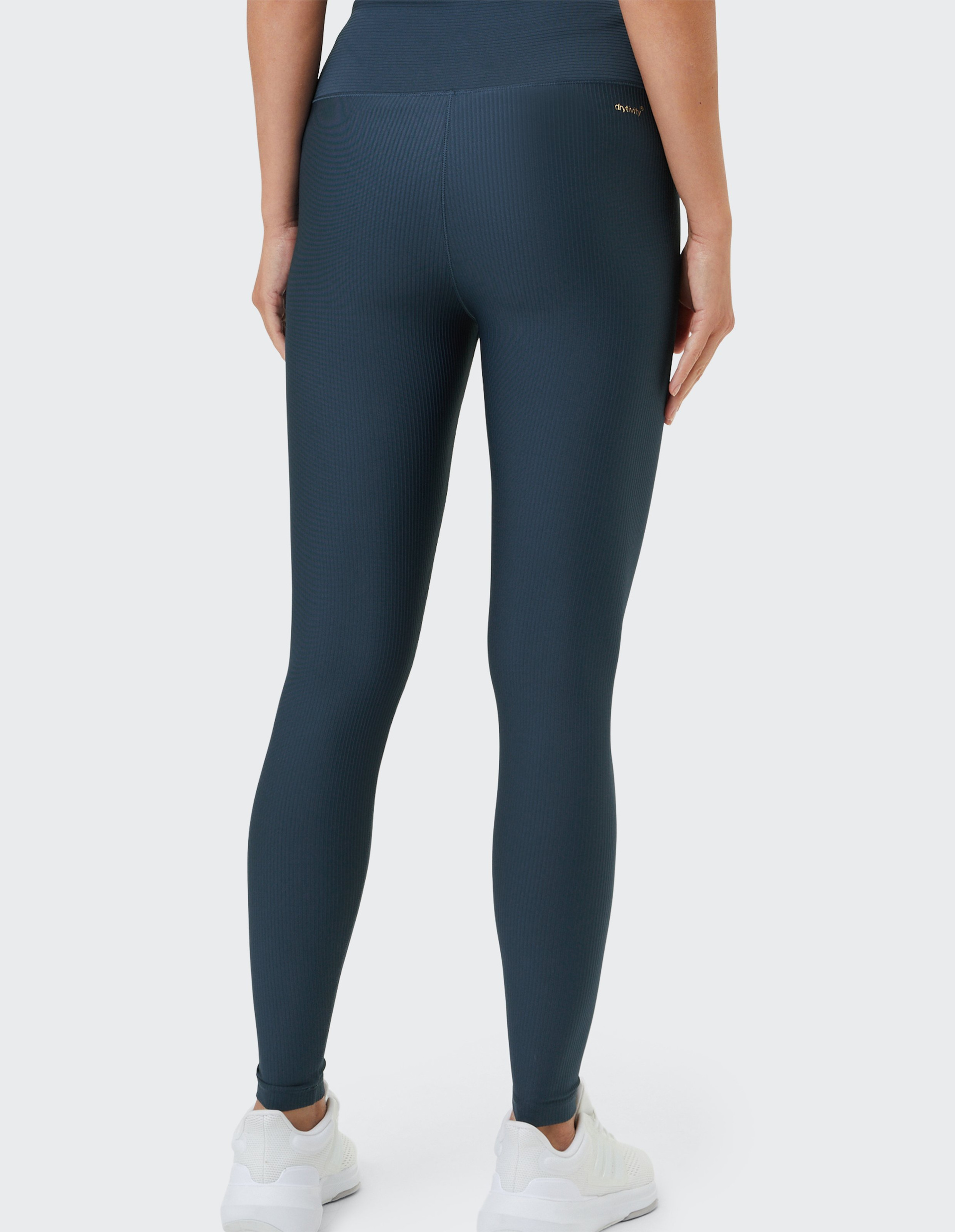 Eine Person in dunkelgrauen Leggings und weißen Sneakers wird von hinten fotografiert, stehend vor einem hellgrauen Hintergrund.