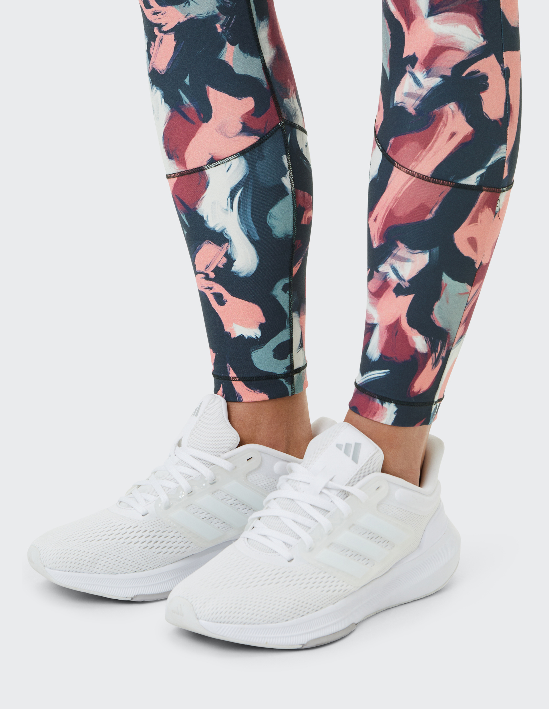 Weiße Turnschuhe mit Schnürsenkeln werden von einer Person getragen, deren Leggings ein buntes, abstraktes Muster hat.
