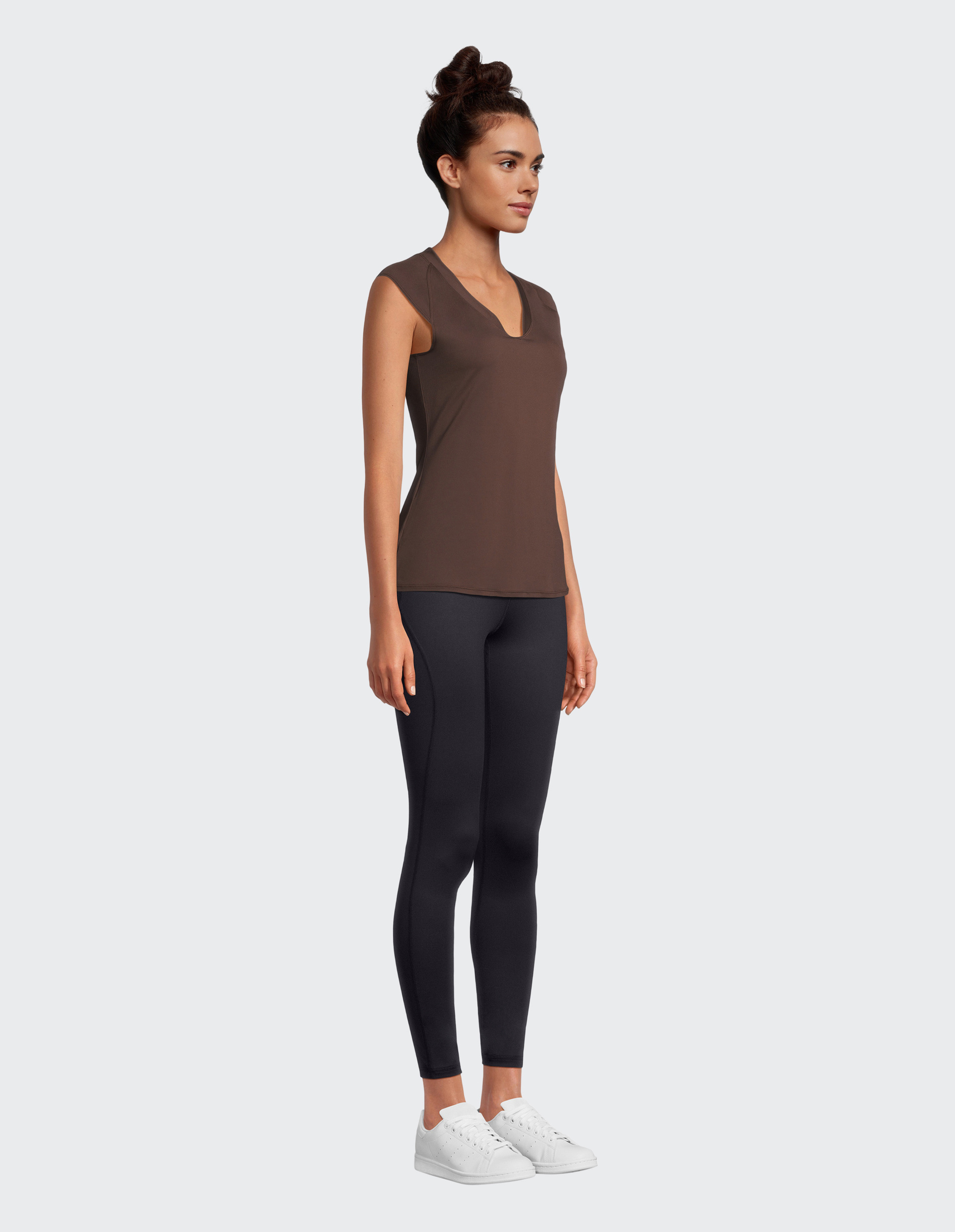 Frau in einem braunen, ärmellosen Oberteil mit V-Ausschnitt und einer schwarzen Leggings.