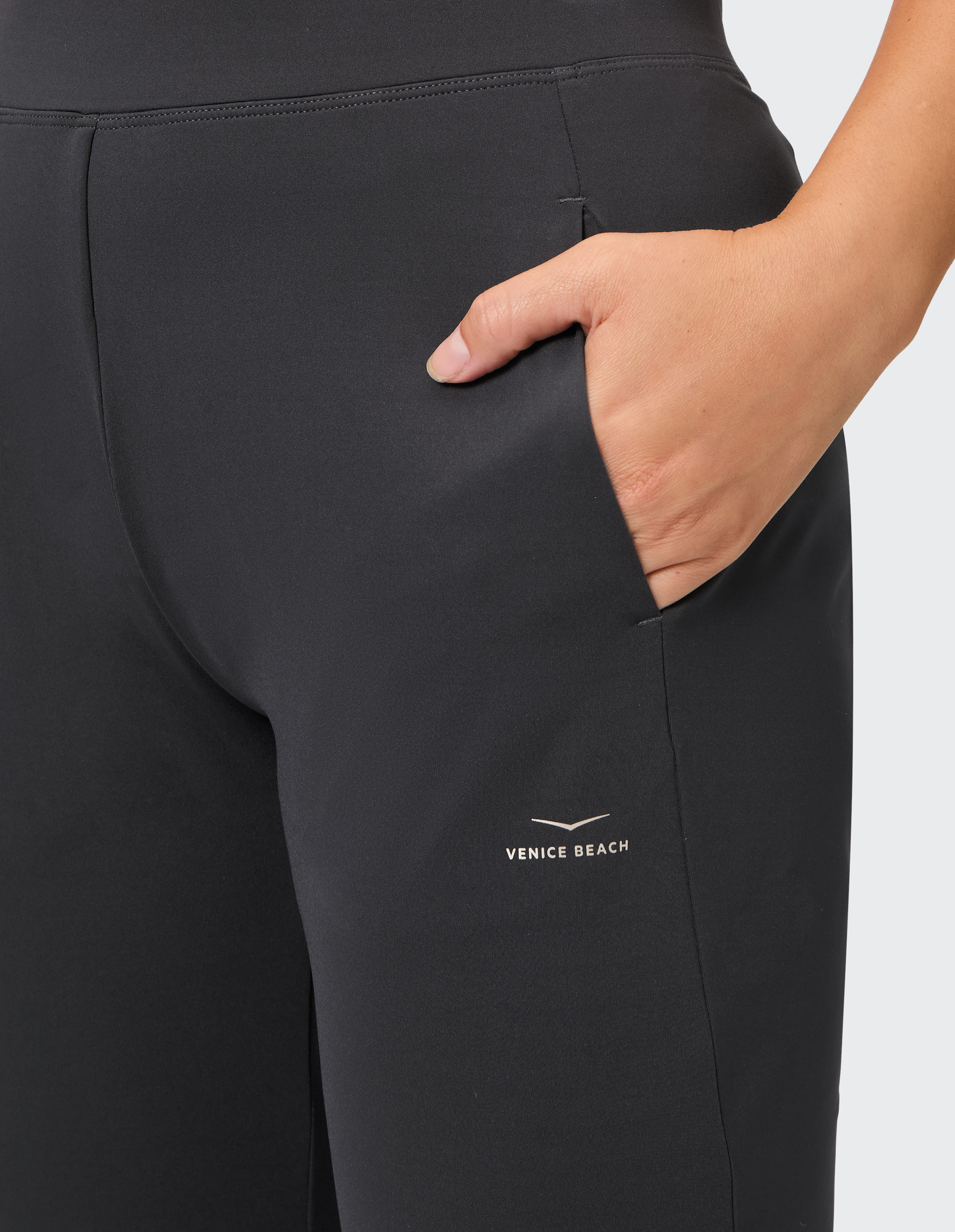 Dunkle Leggings mit eingesteckter Hand in der rechten Tasche, Logo "Venice Beach" sichtbar, auf hellem Hintergrund.