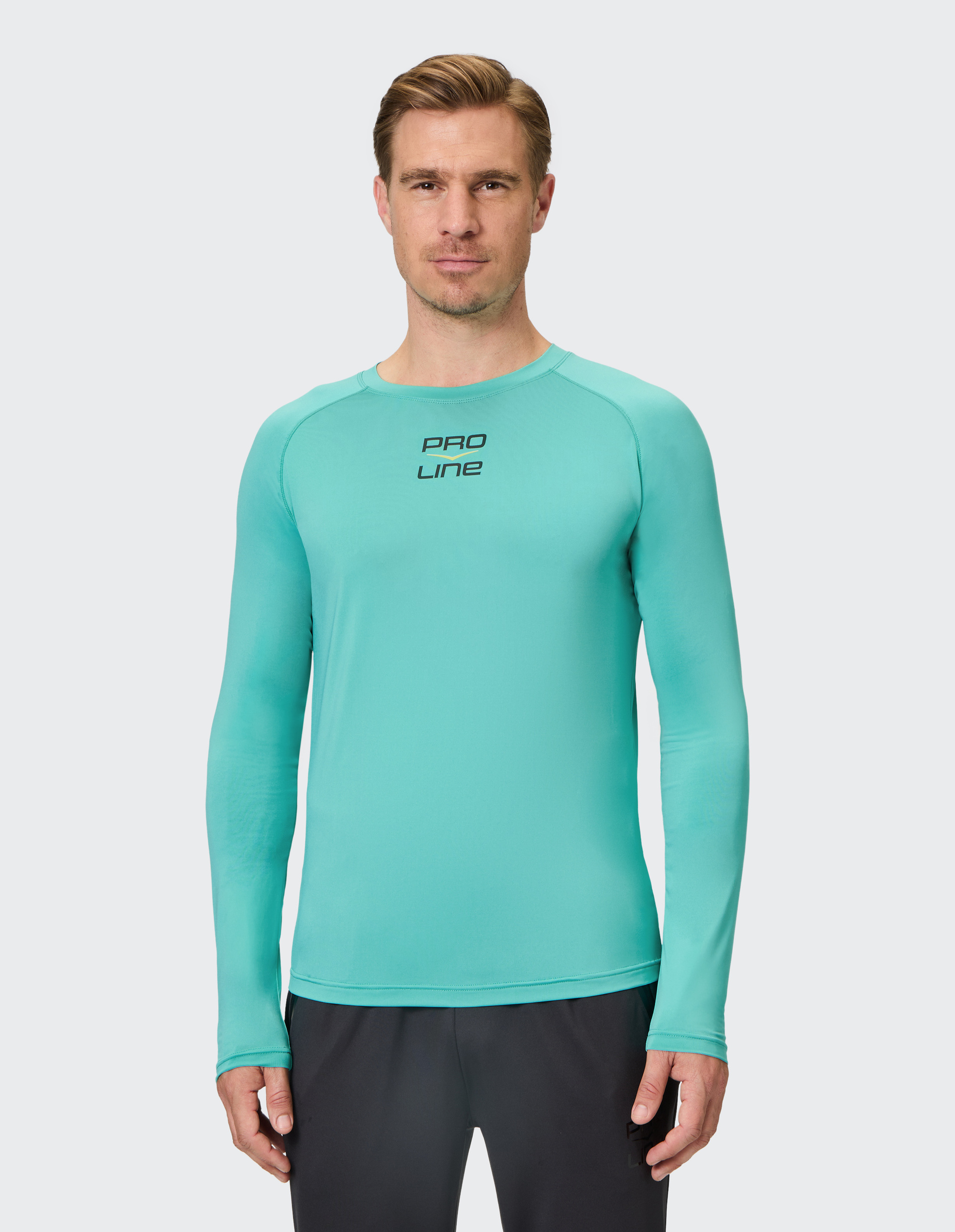 Mann mit blondem Haar trägt ein mintgrünes Langarmshirt mit "PRO LINE"-Logo und schwarze Hose vor hellem Hintergrund.