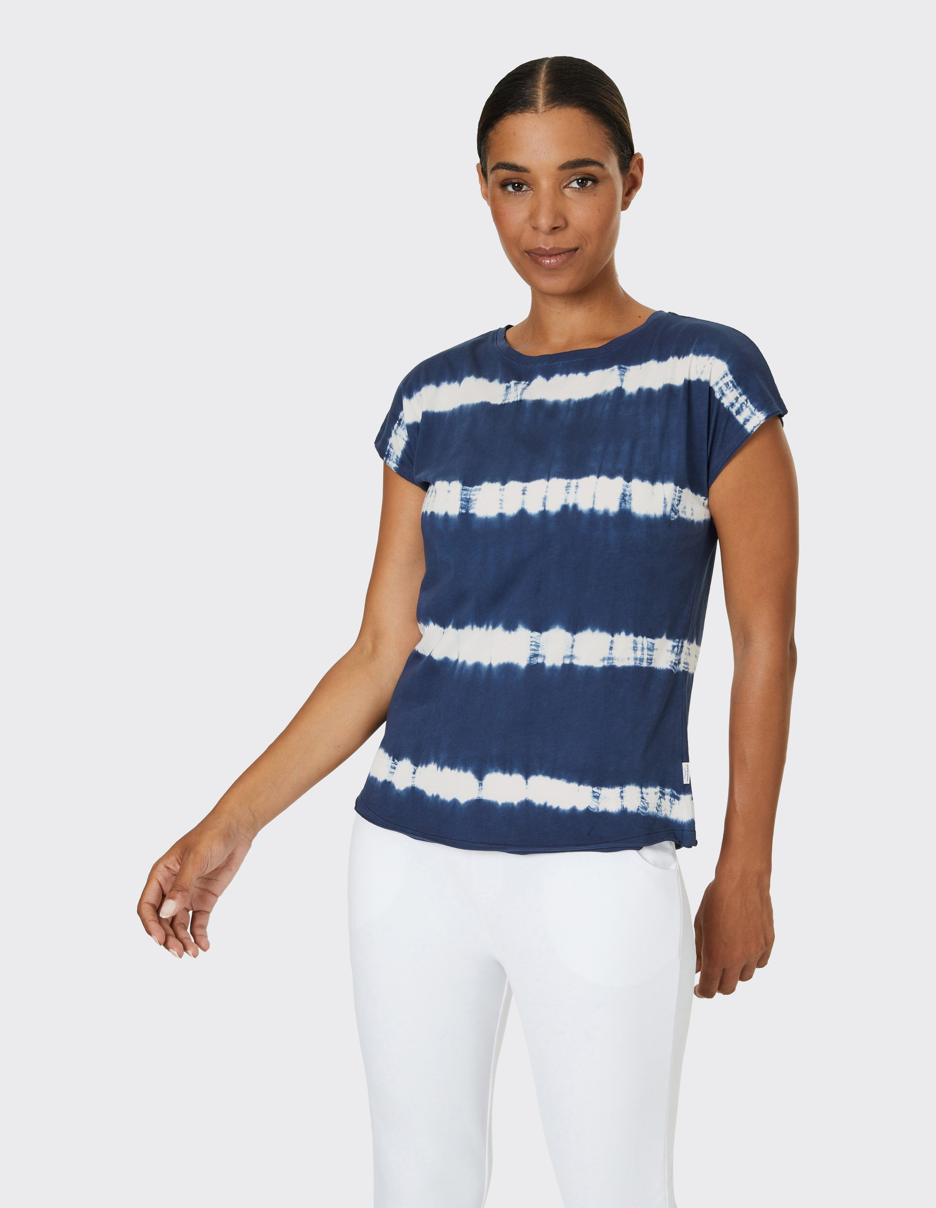 Frau in dunkelblauem Batik-T-Shirt mit weißen Streifen und weißen Hosen.