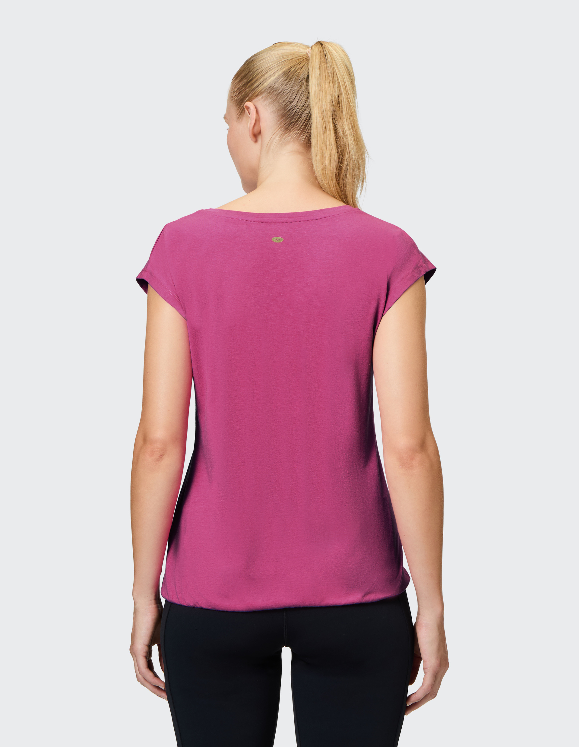 Frau mit blonden Haaren im Pferdeschwanz trägt ein pinkes T-Shirt und schwarze Leggings, von hinten fotografiert.