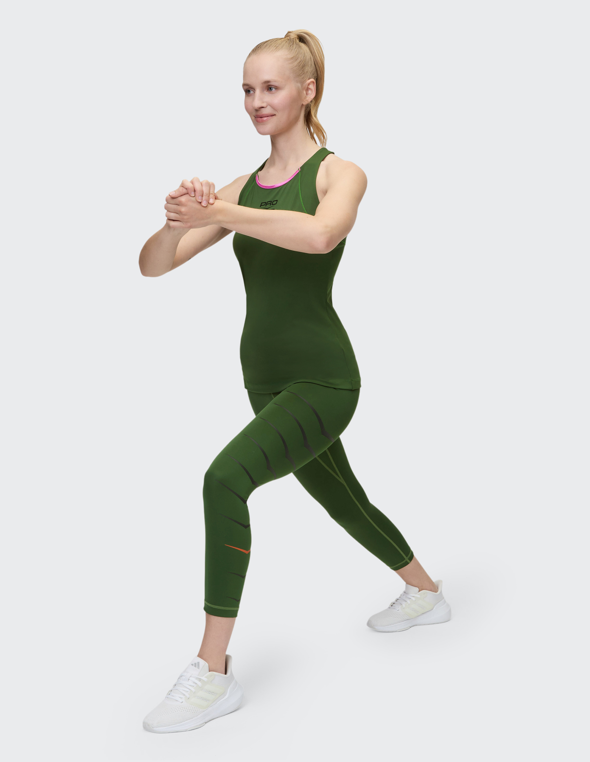 Frau in grüner Sportkleidung macht einen Ausfallschritt, hält ihre Hände zusammen, schaut konzentriert zur Seite.