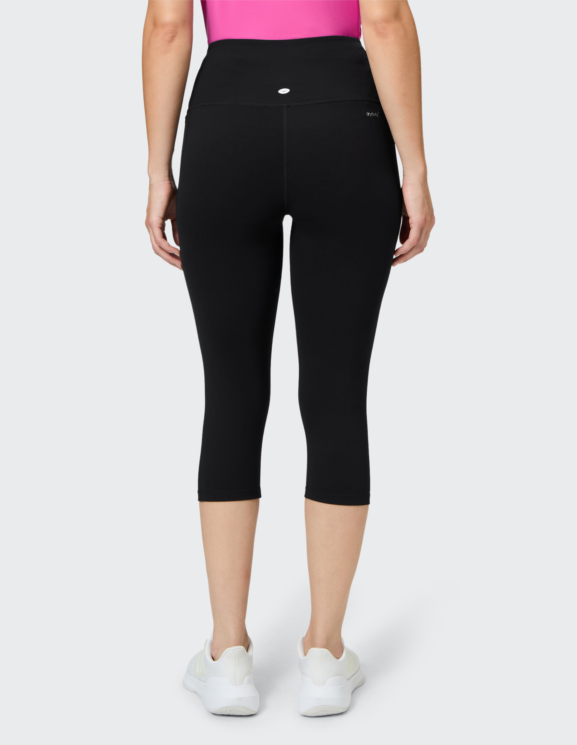 Person von hinten in schwarzer 3/4-Leggings, pinkem Top und weißen Sneakers vor grauem Hintergrund.