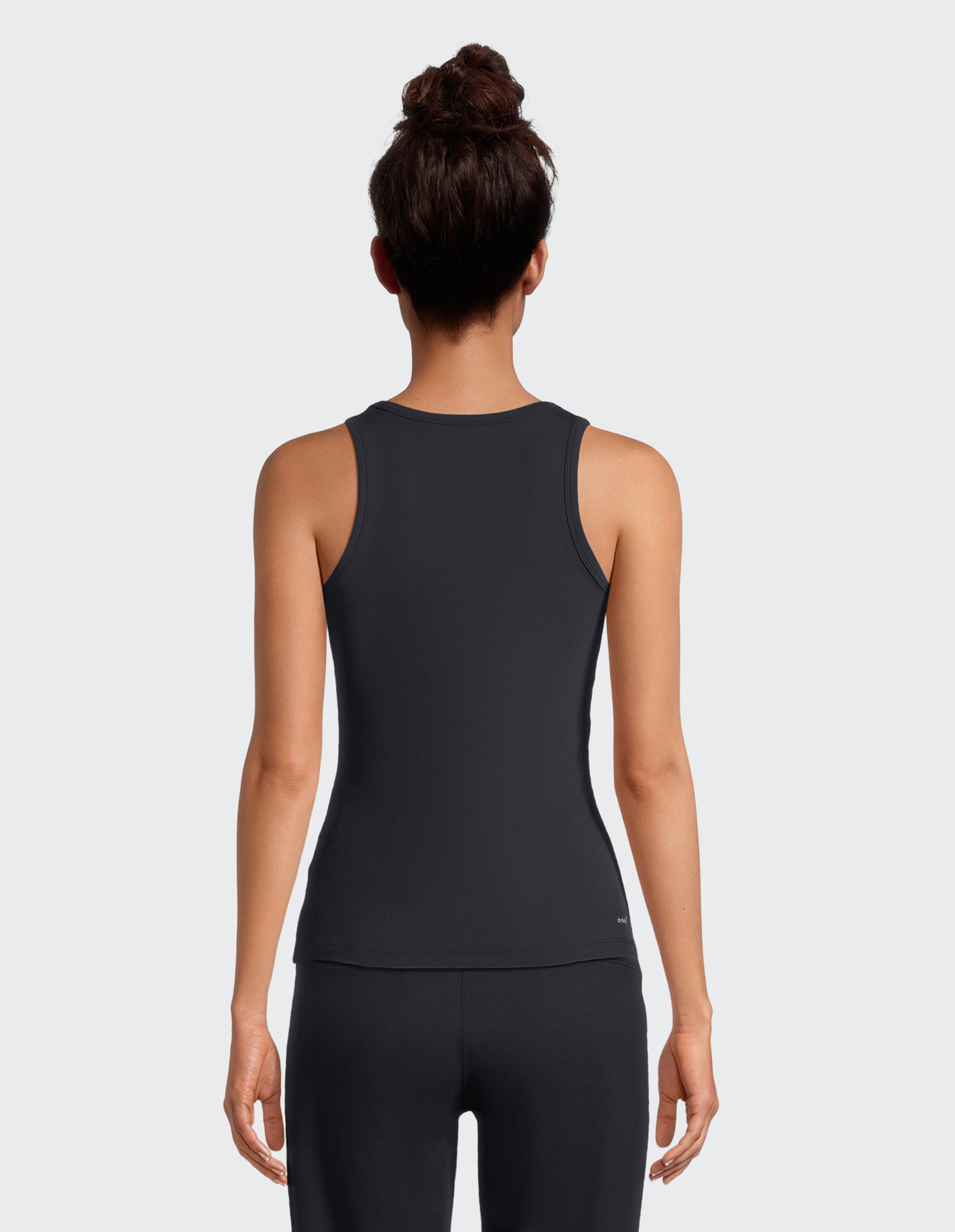 Frau von hinten mit hochgestecktem Haar in einem dunklen ärmellosen Shirt und passender Hose vor grauem Hintergrund.