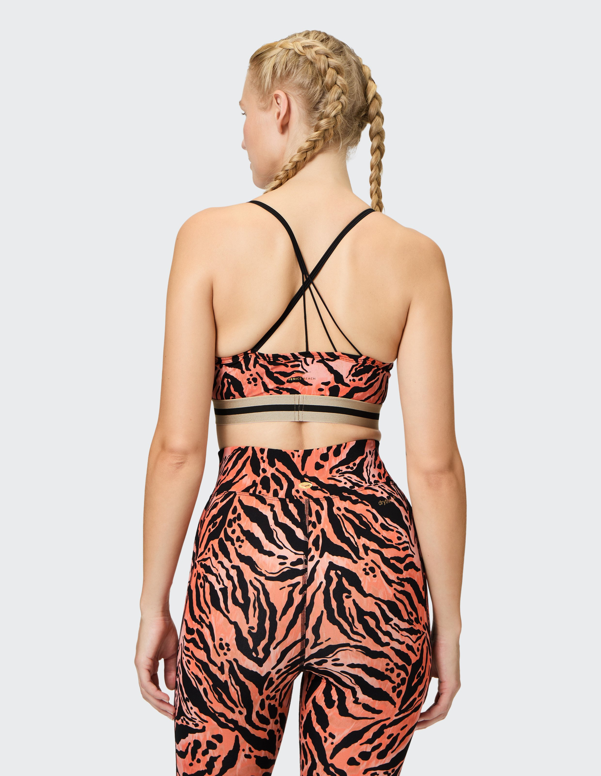 Eine Frau mit geflochtenem Haar trägt einen Sport-BH und Leggings mit schwarzem und orangefarbenem Tigerstreifenmuster.