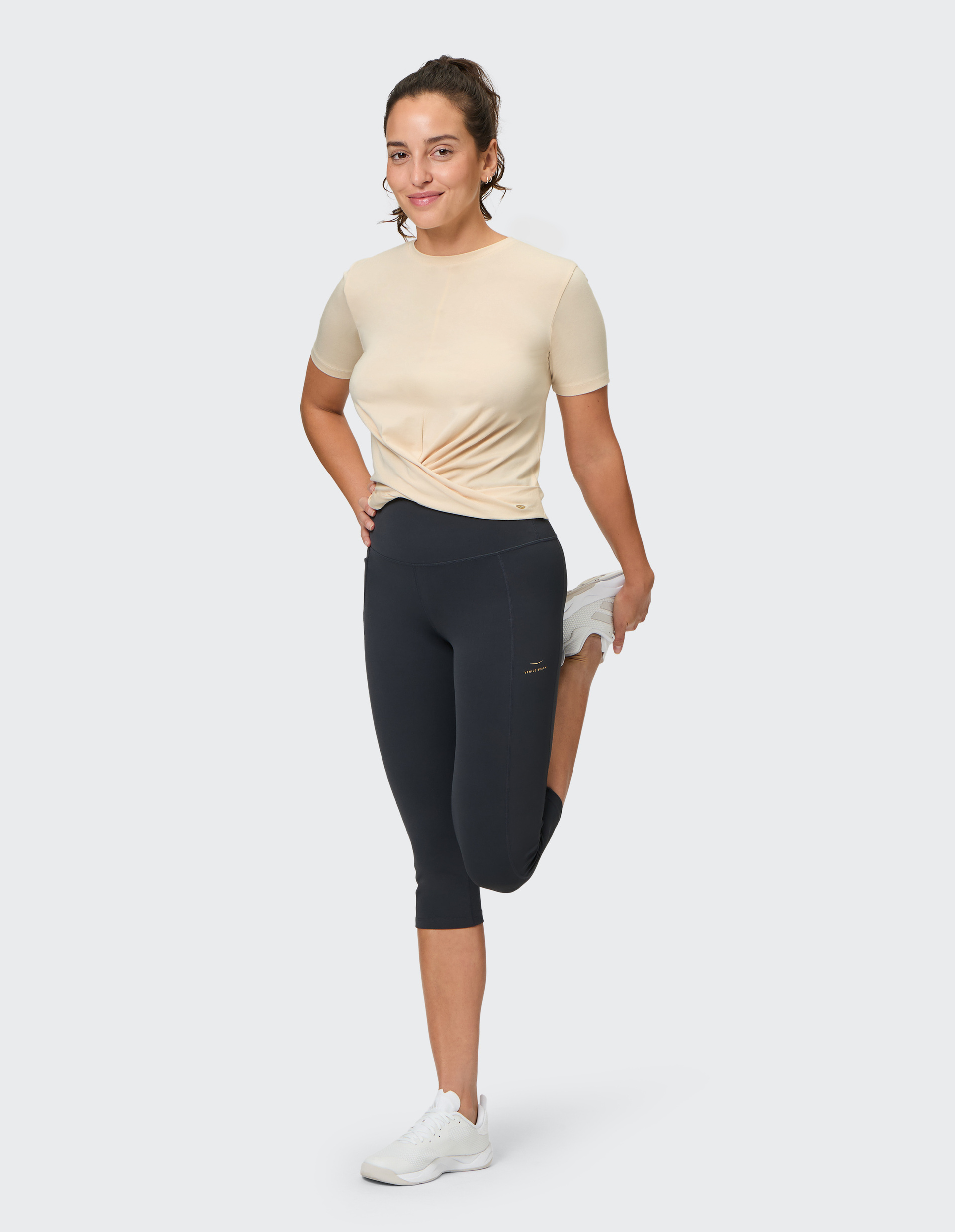 Beiges T-Shirt mit kurzen Ärmeln und einem dekorativen Knoten unterhalb der Taille, aus leichtem und dehnbarem Stoff.