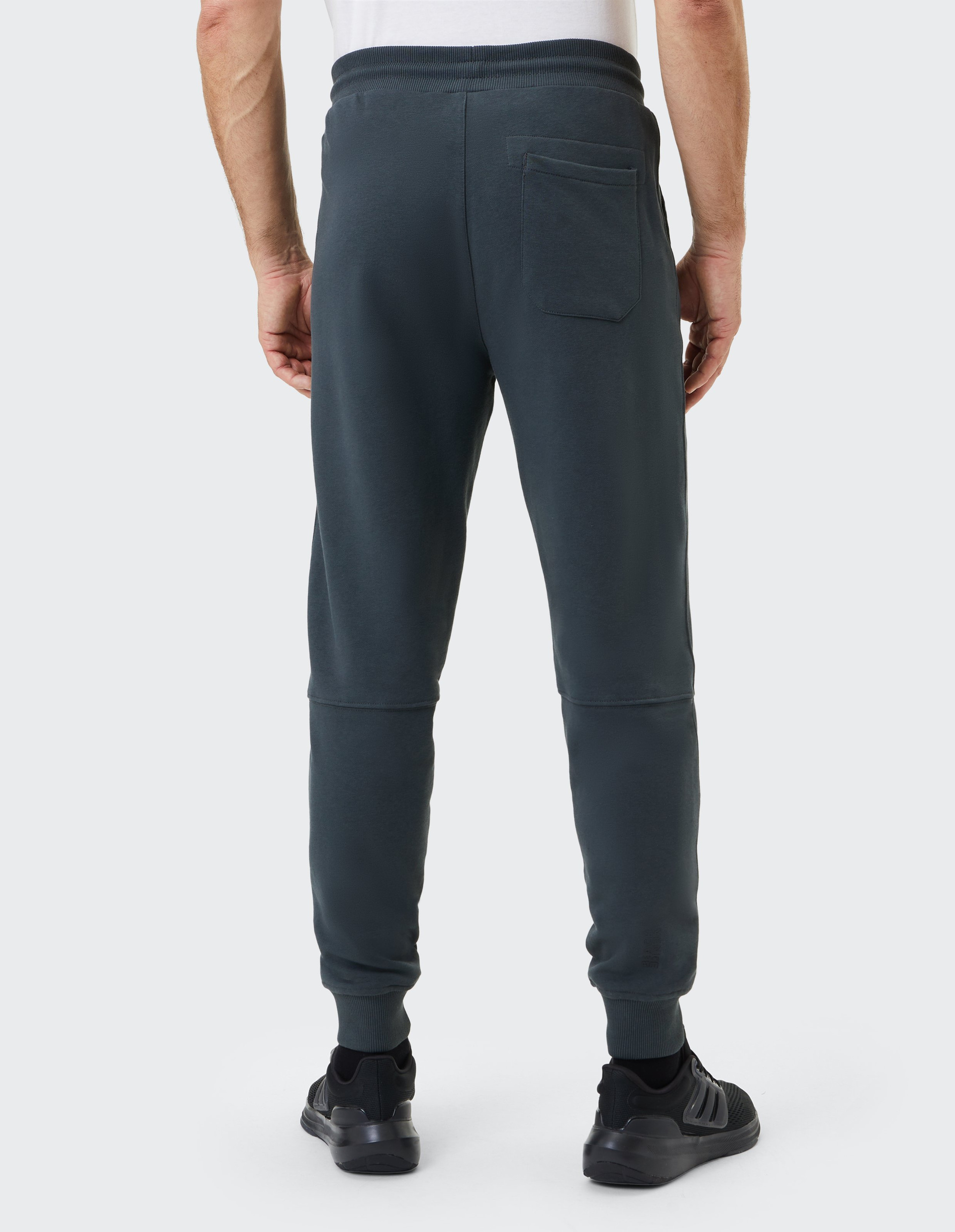 Ein Mann steht mit dem Rücken zur Kamera und trägt eine dunkelgraue Jogginghose mit einer Gesäßtasche und schwarze Turnschuhe.