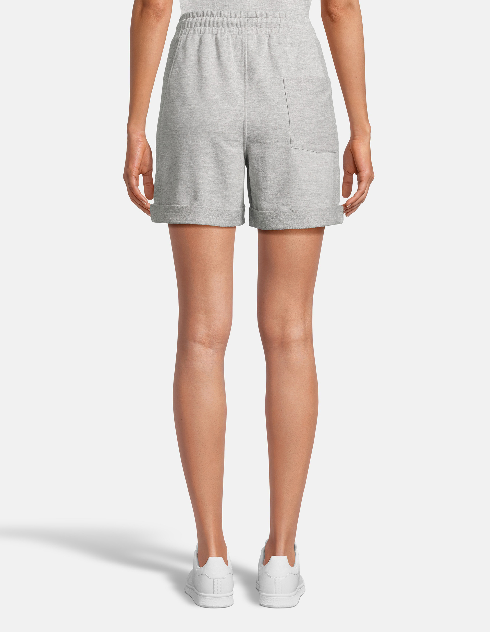 Eine Person in grauen Shorts mit Gummizug und Tasche, steht mit dem Rücken zur Kamera, trägt weiße Turnschuhe auf weißem Hintergrund.