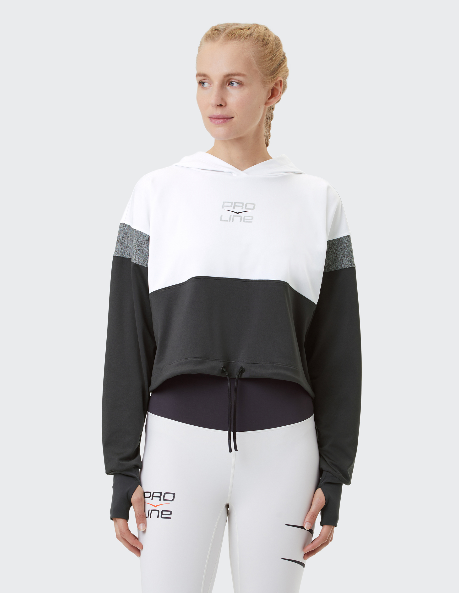 Frau in schwarz-weißem Sportoutfit mit Kapuzenpullover und Leggings von Pro Line, schaut zur Seite vor grauem Hintergrund.