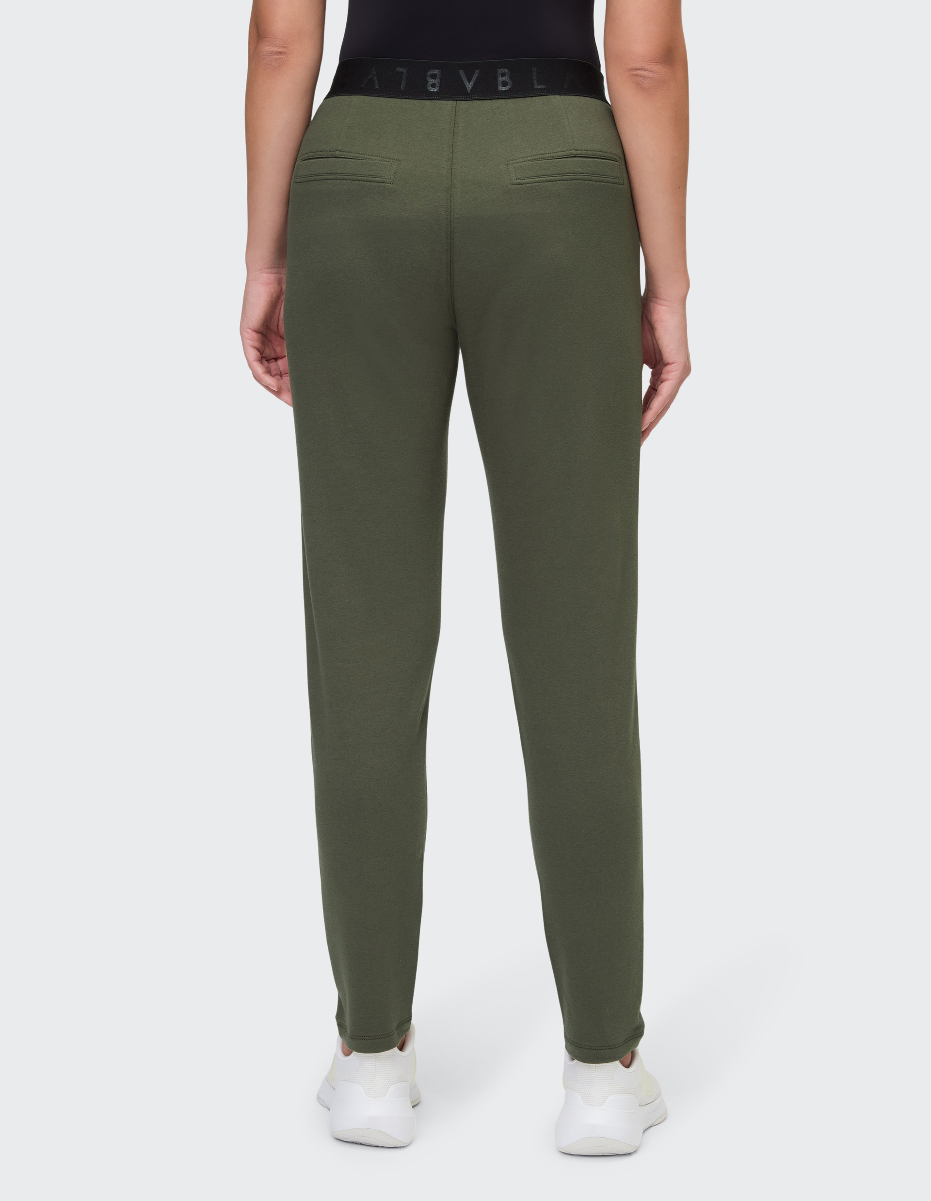 Person in olivgrüner Hose und weißem Sneaker, schwarze Oberbekleidung; Hose hat zwei Gesäßtaschen und einen schwarzen Bund.