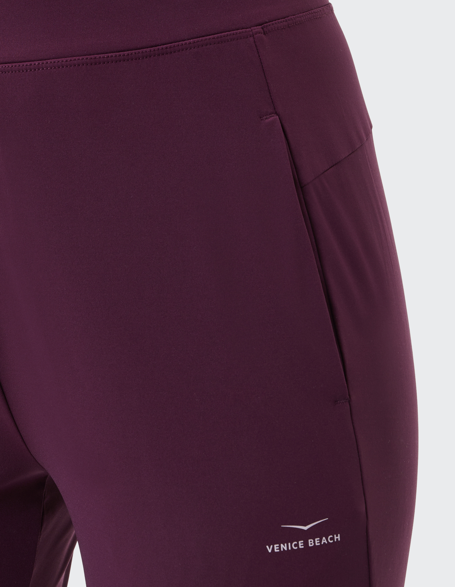 Nahaufnahme einer dunkelvioletten Sportleggings mit glattem Stoff und markanten Nähten, seitlich mit der Aufschrift "Venice Beach".