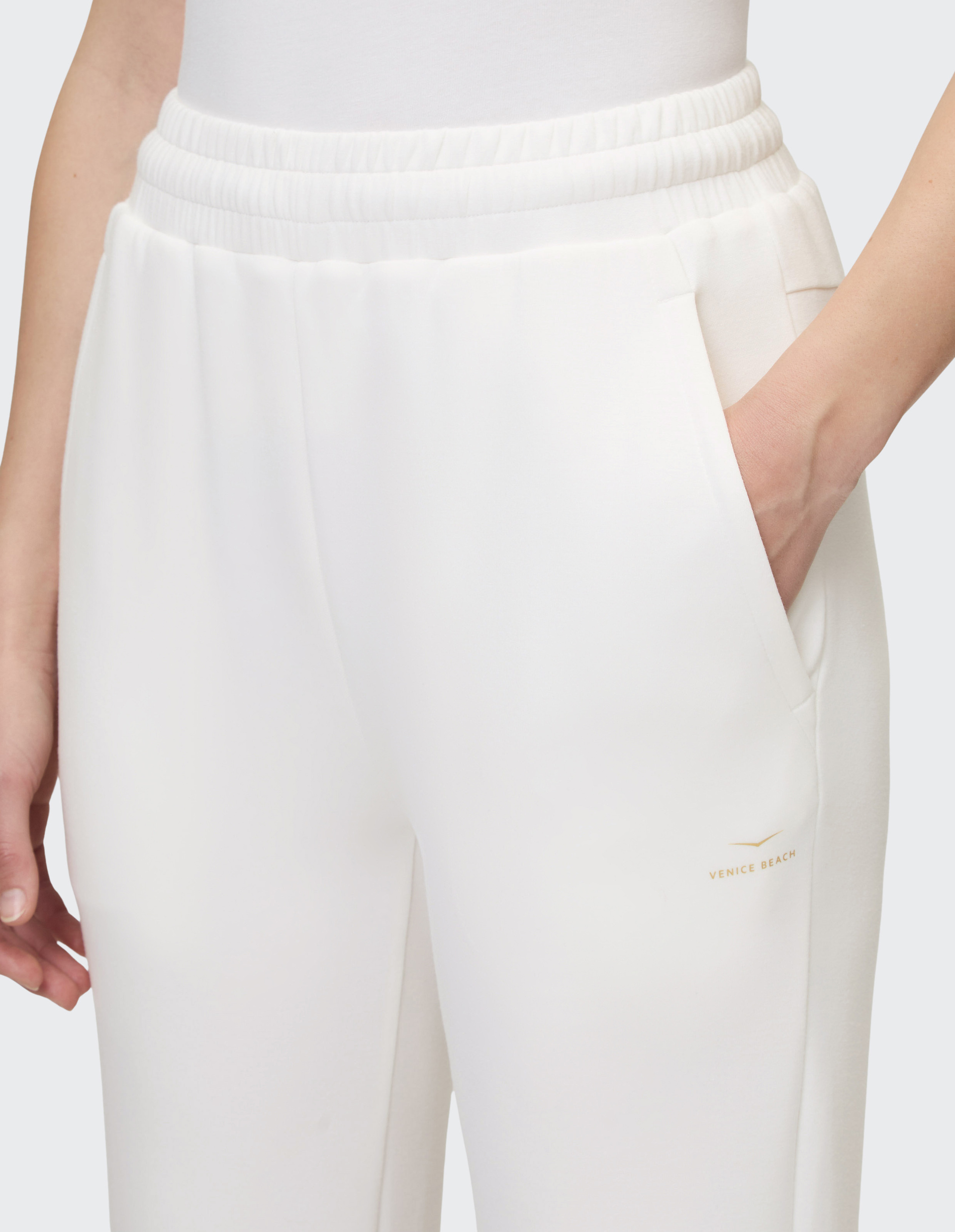 Weiße Jogginghose mit elastischem Bund, rechte Hand in der Hosentasche, dezentes "Venice Beach"-Logo oberhalb des Oberschenkels.