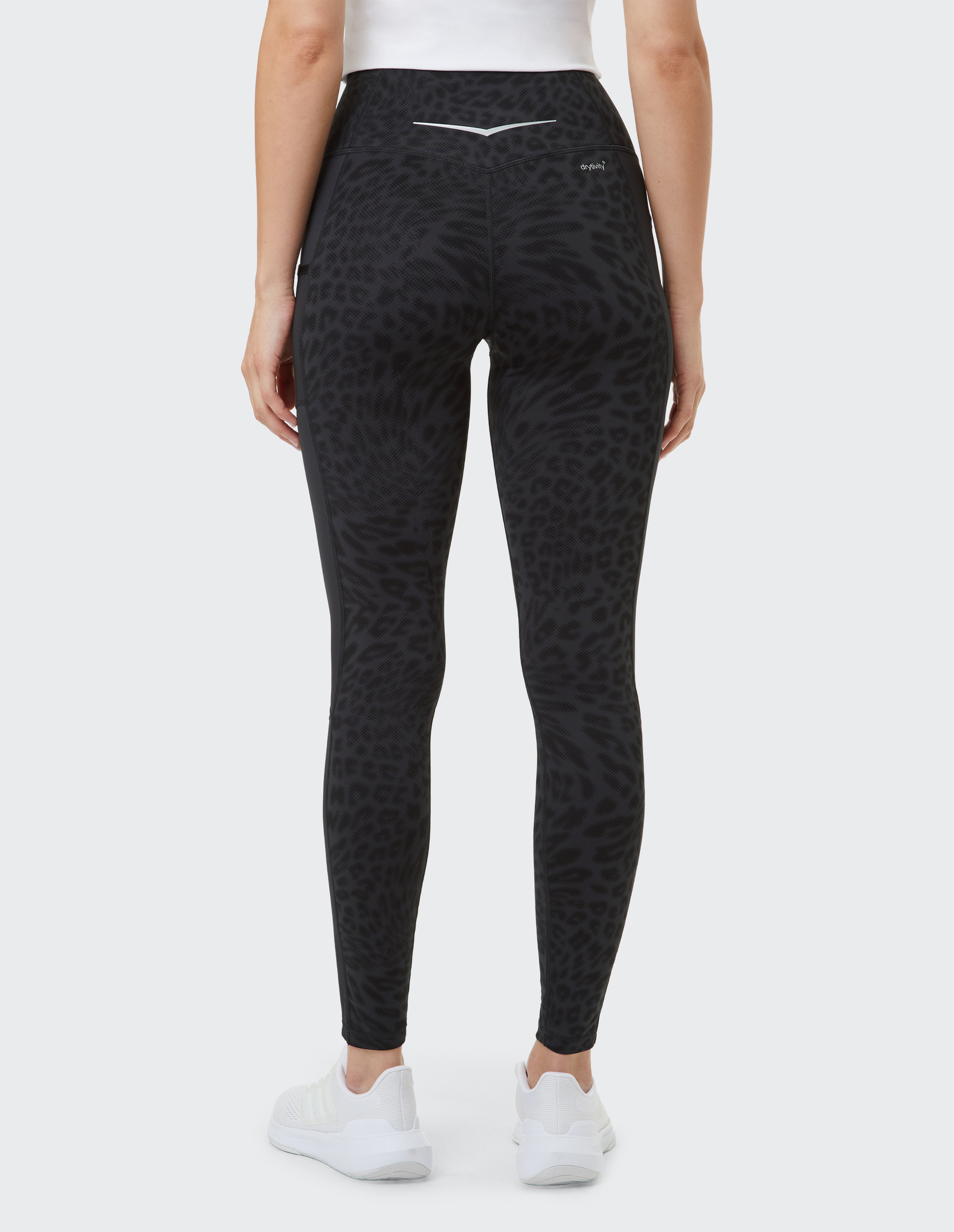 Person in schwarzer Leggings mit Leopardenmuster von hinten, trägt weiße Sportschuhe und ein weißes Oberteil, auf hellem Hintergrund.
