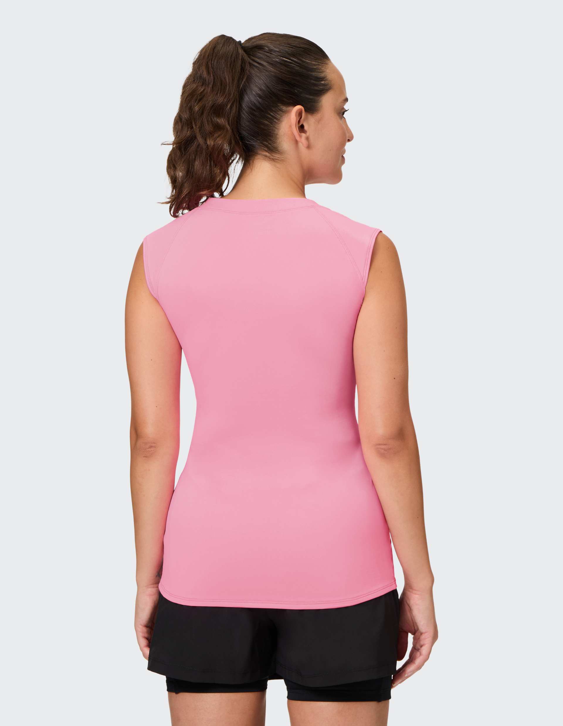 Frau in rosa ärmellosem Oberteil und schwarzen Shorts, von hinten, mit einem lockigen Pferdeschwanz, zeigt muskulösen Rücken.