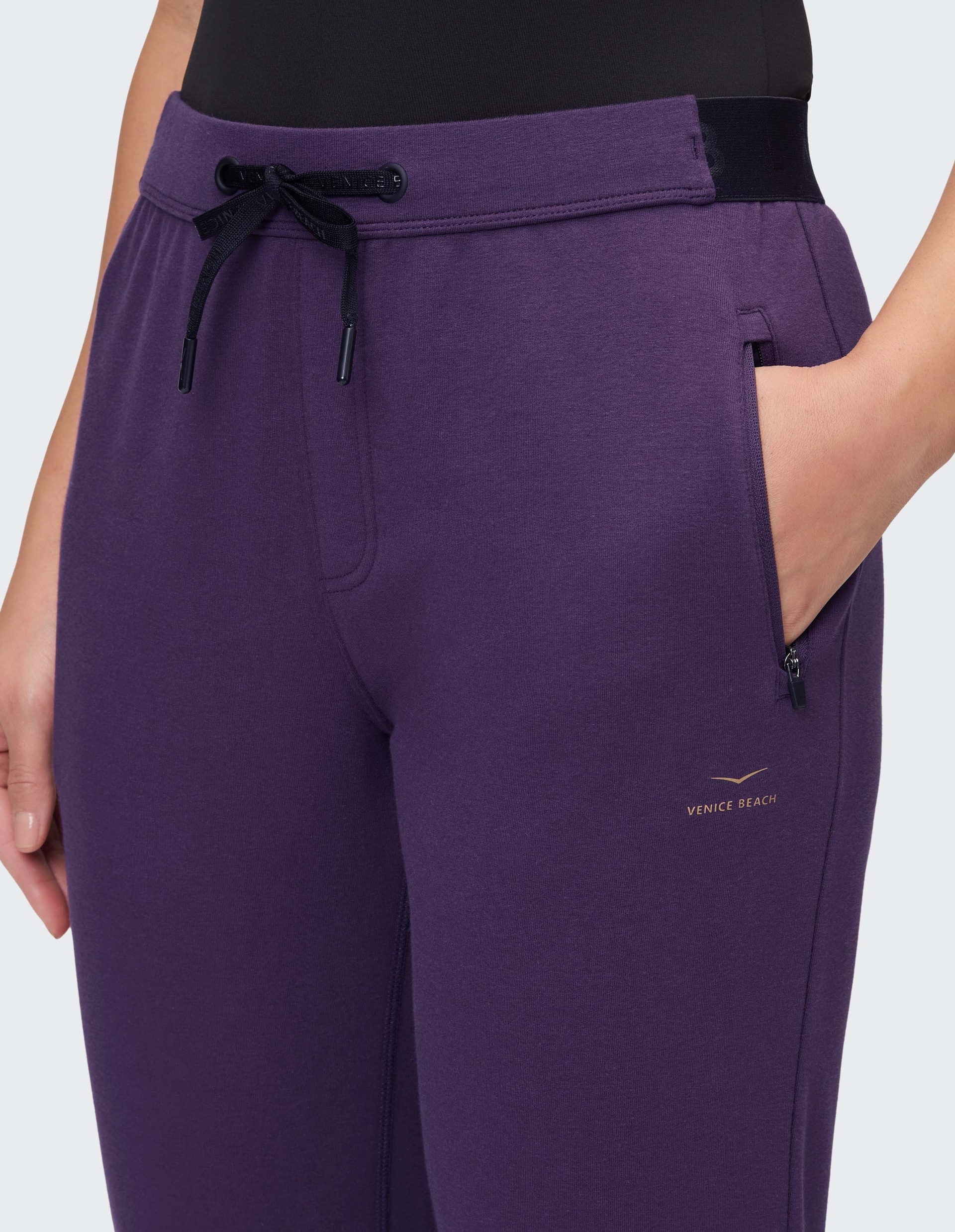Lila Jogginghose mit schwarzem Kordelzug, Reißverschlusstasche und Logo "Venice Beach", von einem Modell getragen.