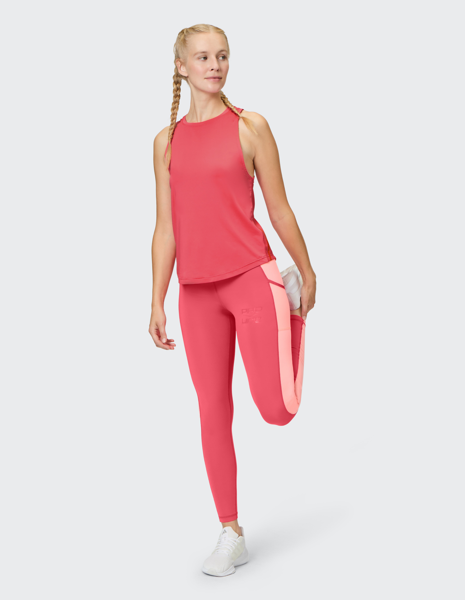 Eine Frau in rosa Sportbekleidung dehnt ihr Bein, während sie auf einem Fuß steht und den anderen hinter sich anhebt.