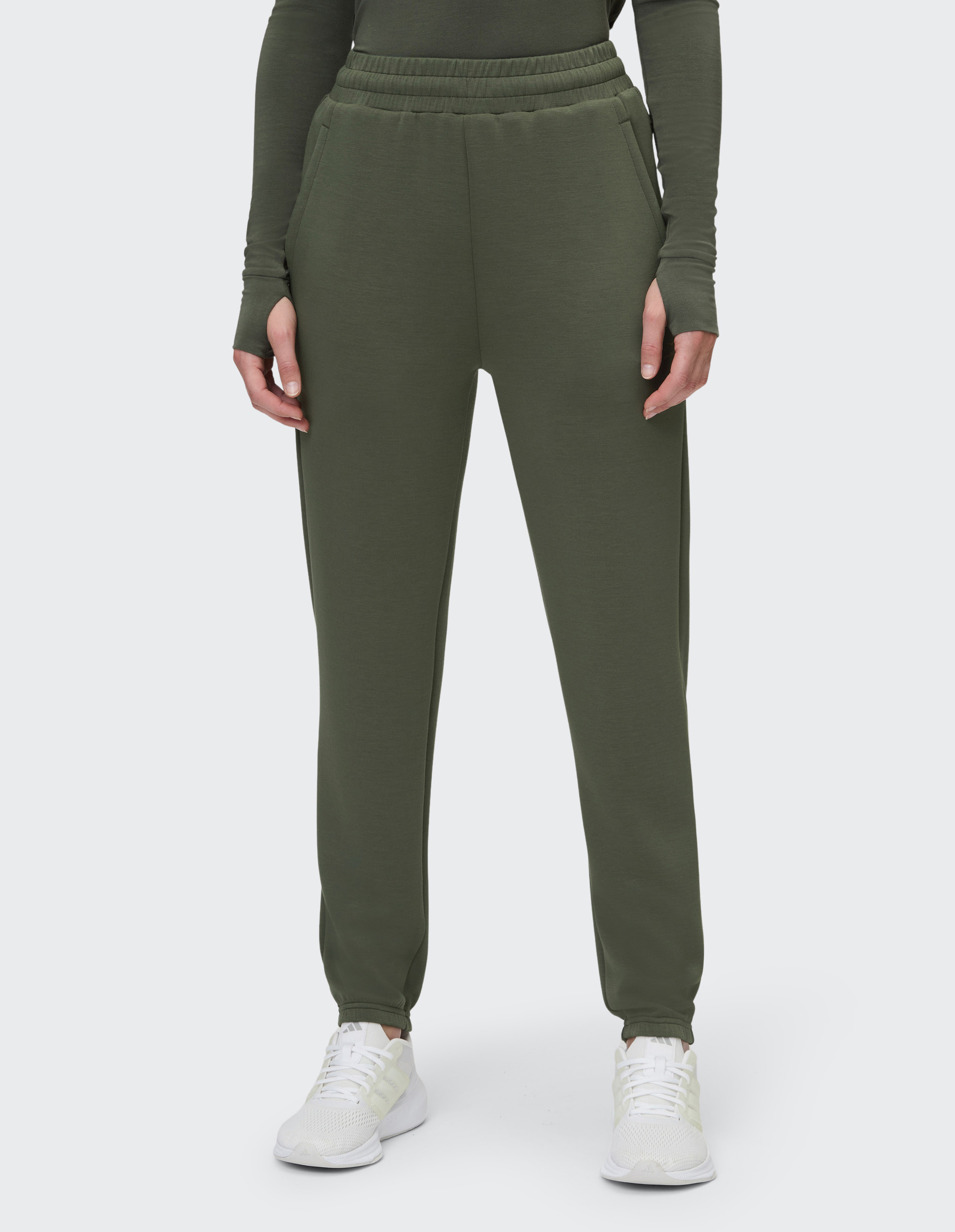Person in olivgrüner Jogginghose mit elastischem Bund und verdeckten Taschen, dazu passende olivgrüne Oberbekleidung und weiße Turnschuhe.