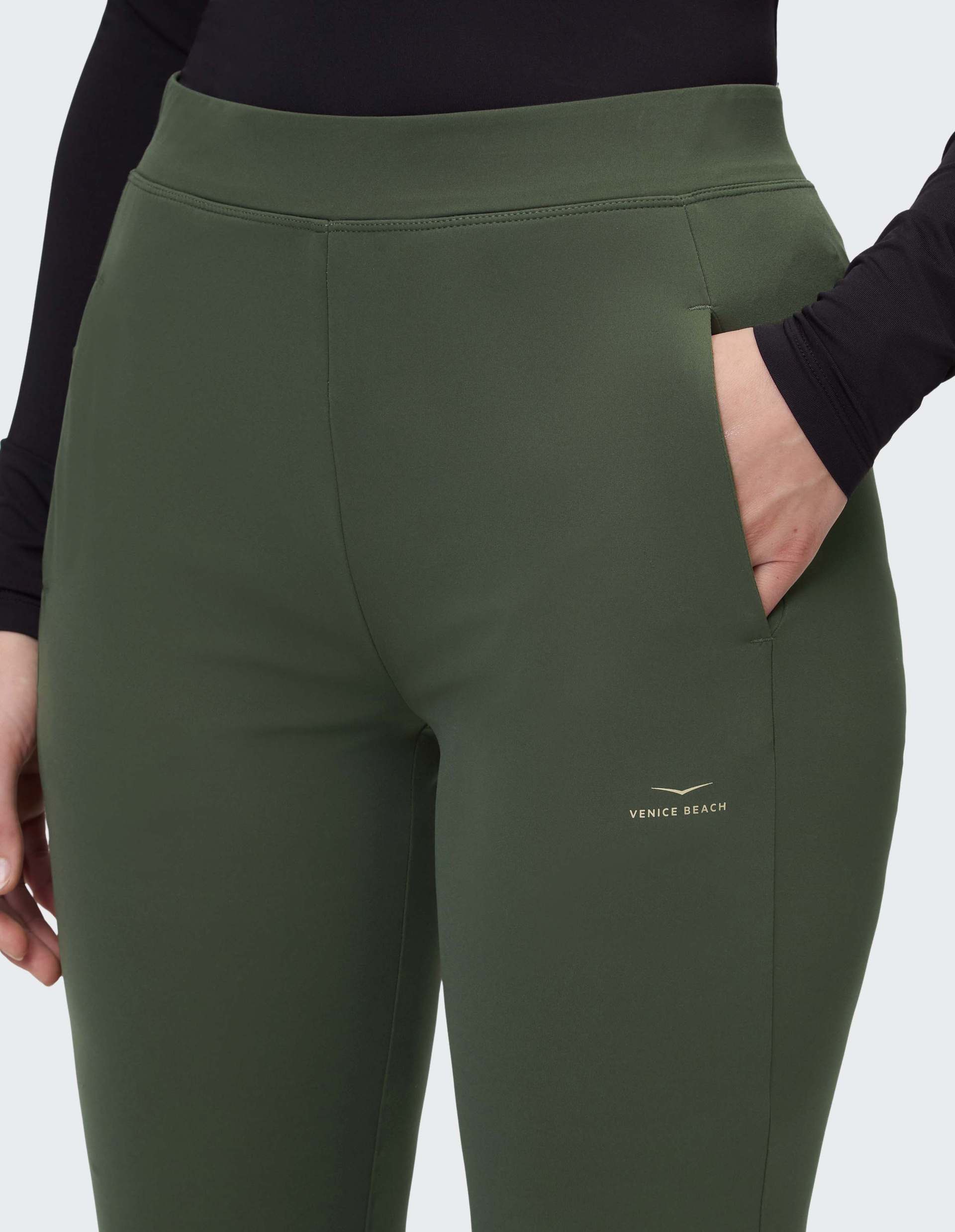 Person trägt dunkelgrüne Leggings mit Eingrifftaschen und Venice Beach-Logo, kombiniert mit schwarzem Langarmshirt.